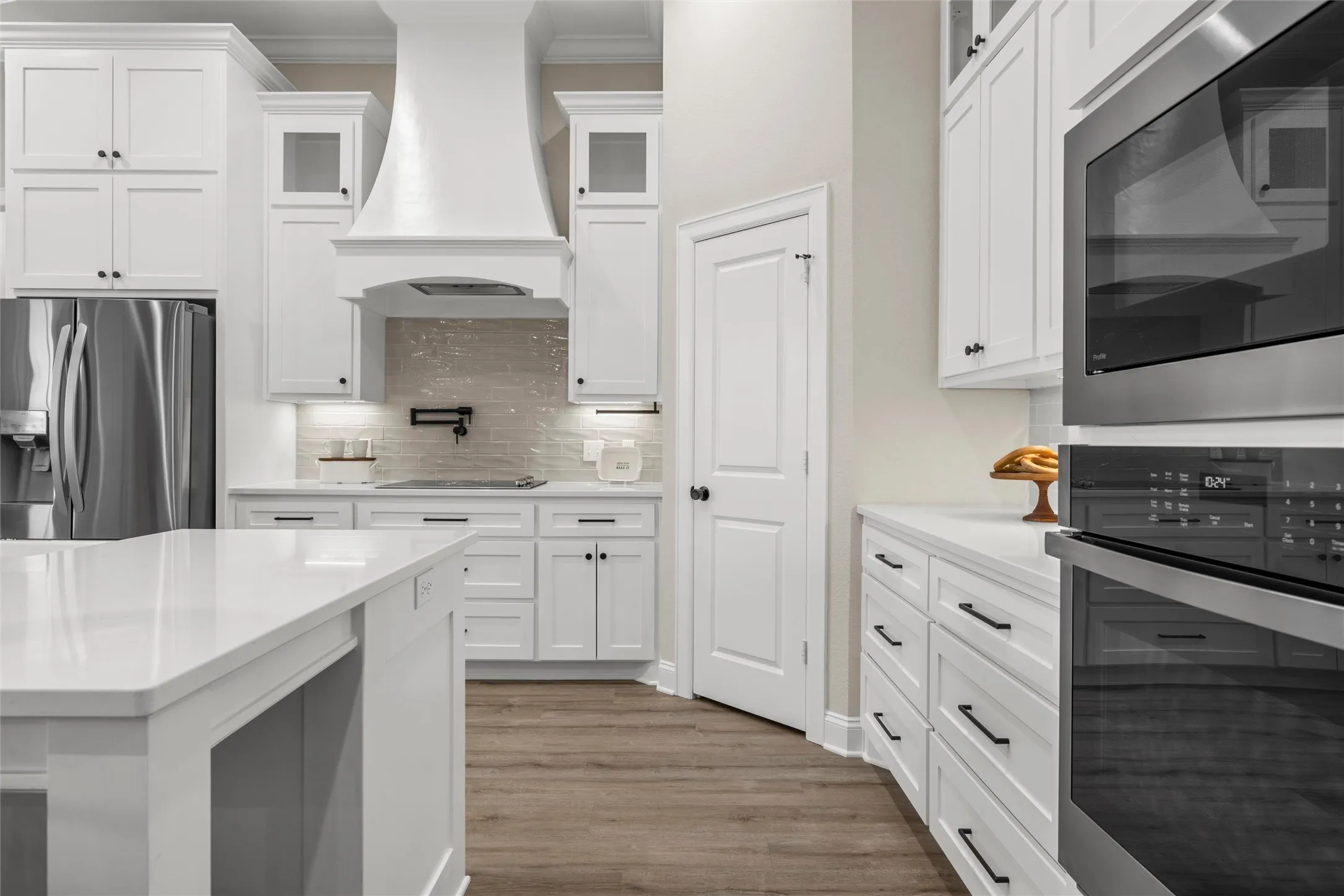 White shaker cabinetry, quartz countertops, stainless steel appliances, wood-finish flooring, and a decorative range hood