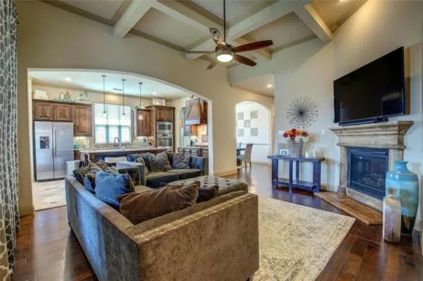 Vaulted ceiling with exposed beams and ceiling fan, wood-finish flooring, fireplace with stone surround, arched doorways, and kitchen with stainless steel appliances and wood cabinetry