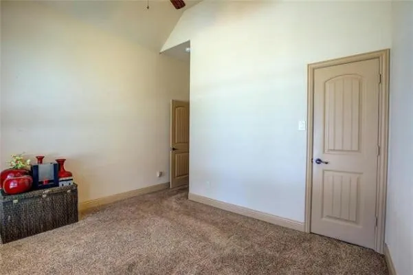 Vaulted ceiling with exposed wood beams, neutral tone carpet, and a solid panel interior door