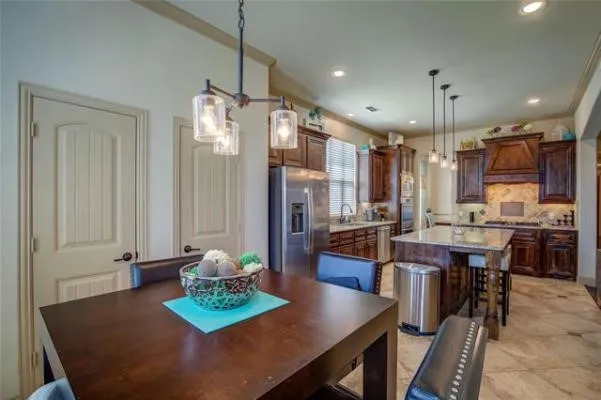 Kitchen with dark wood cabinetry, stainless steel appliances, a large center island with pendant lighting, and tiled flooring