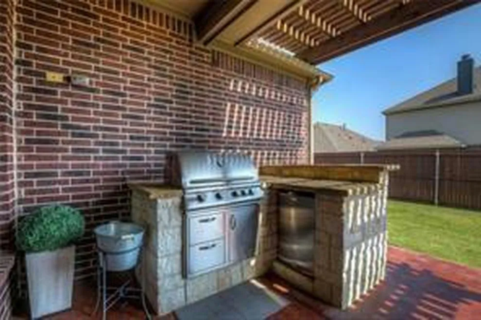 Outdoor kitchen featuring a built-in stainless steel grill, stone-look surround, and integrated countertop space