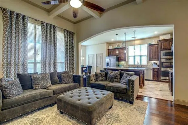 Living area featuring high ceilings with beam accents and a ceiling fan, hardwood flooring, and an arched entryway to the kitchen