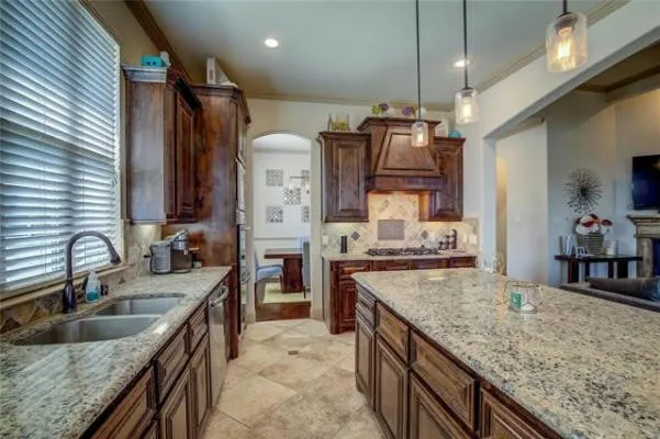 Kitchen featuring dark wood cabinetry, light-colored granite countertops, a double basin stainless steel sink, tile backsplash, and recessed lighting