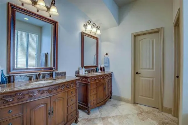 Dual vanity with carved wood cabinetry, stone countertops, and integrated sinks
