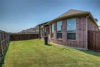 Expansive grass lawn, full perimeter wood fencing, brick exterior, and multiple windows