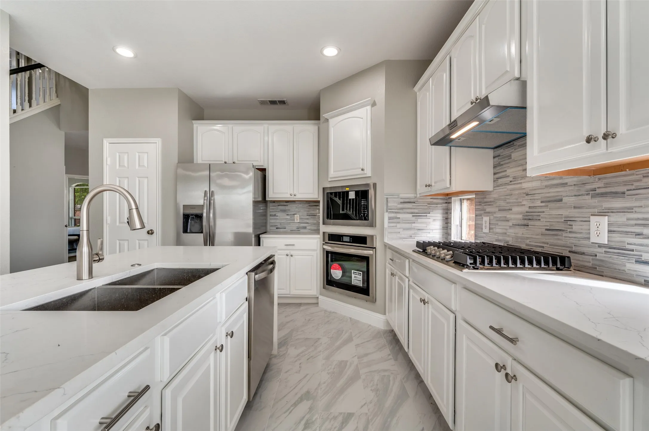 White cabinetry, stainless steel appliances, dual basin sink, integrated cooktop, and patterned tile backsplash