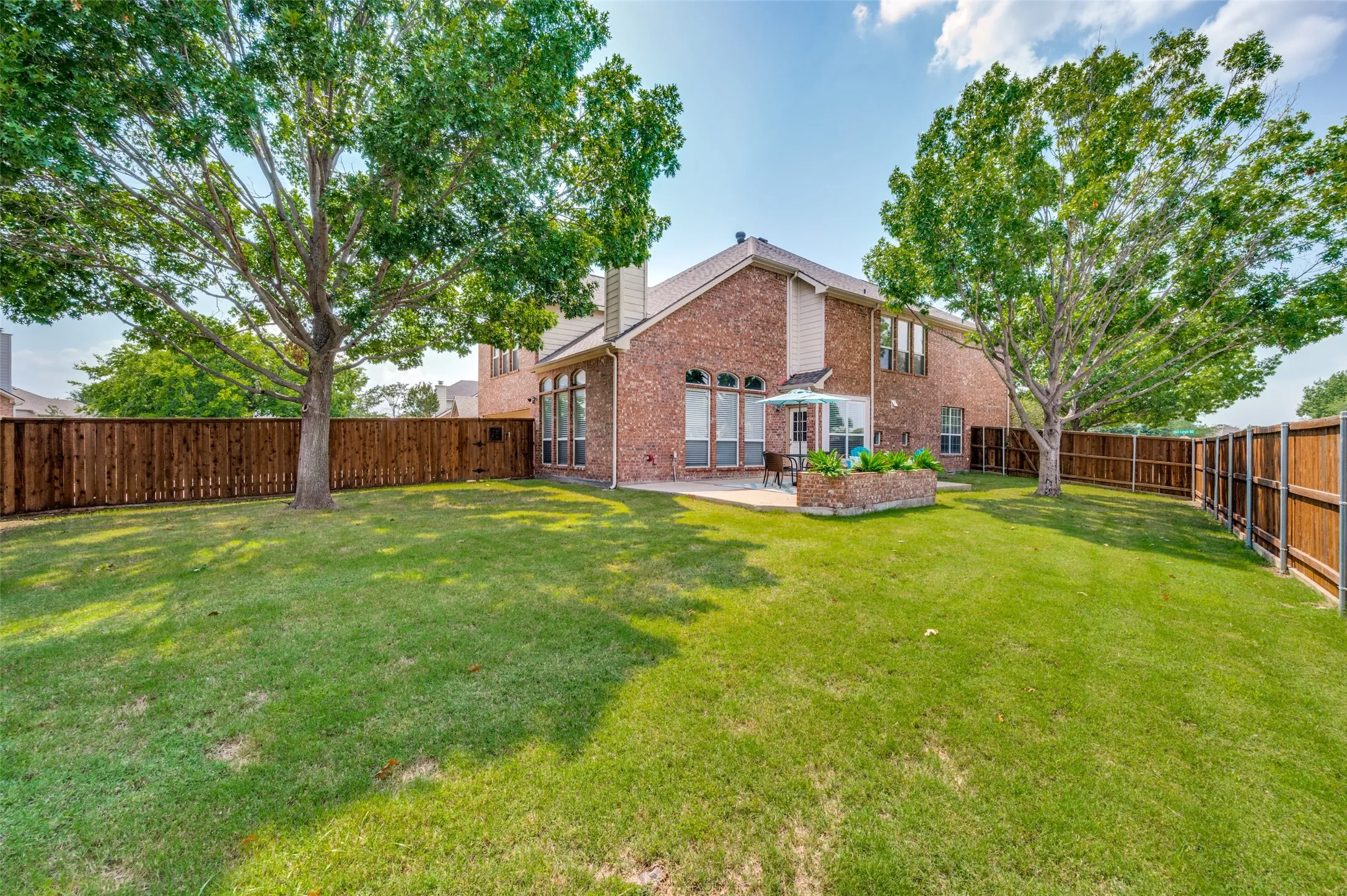 Expansive lawn featuring mature trees and a privacy fence