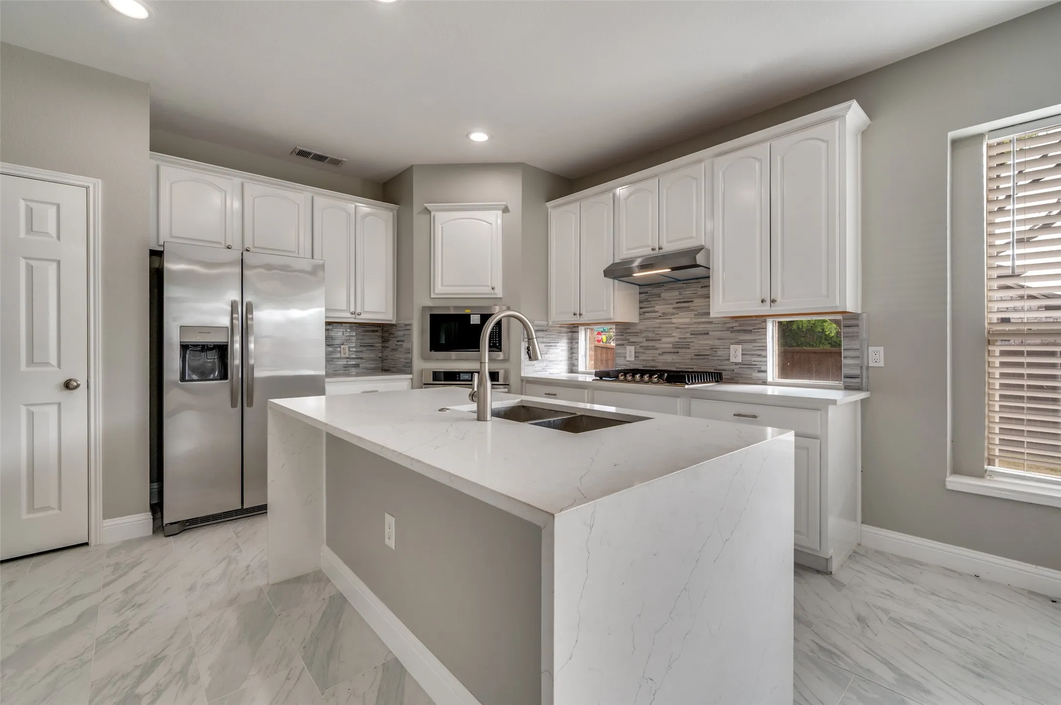 Kitchen featuring white cabinetry, stainless steel appliances, a center island with a built-in sink, and tile flooring
