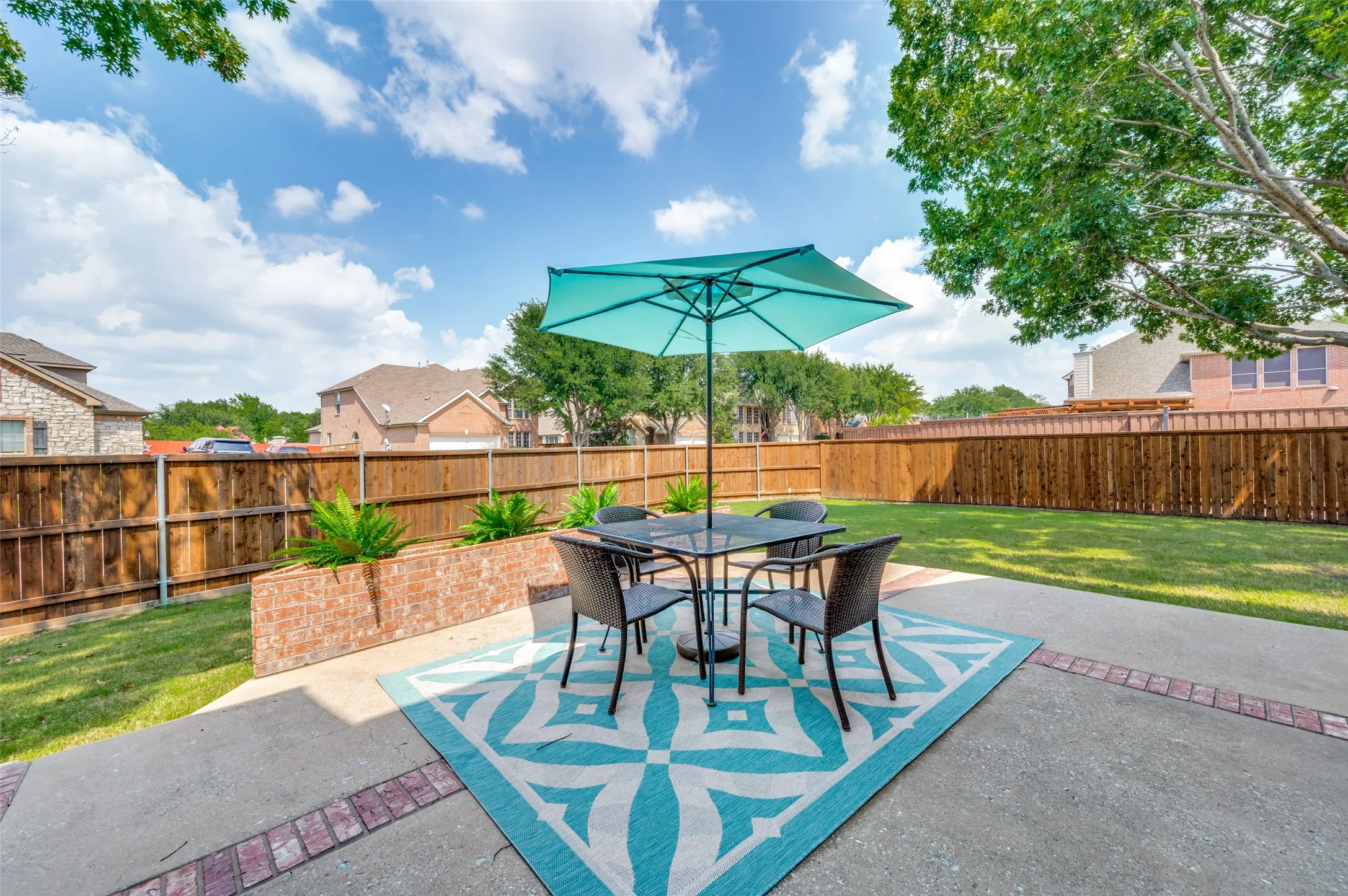 Expansive backyard featuring a concrete patio with brick accents, a raised brick planter, mature trees, and a privacy fence