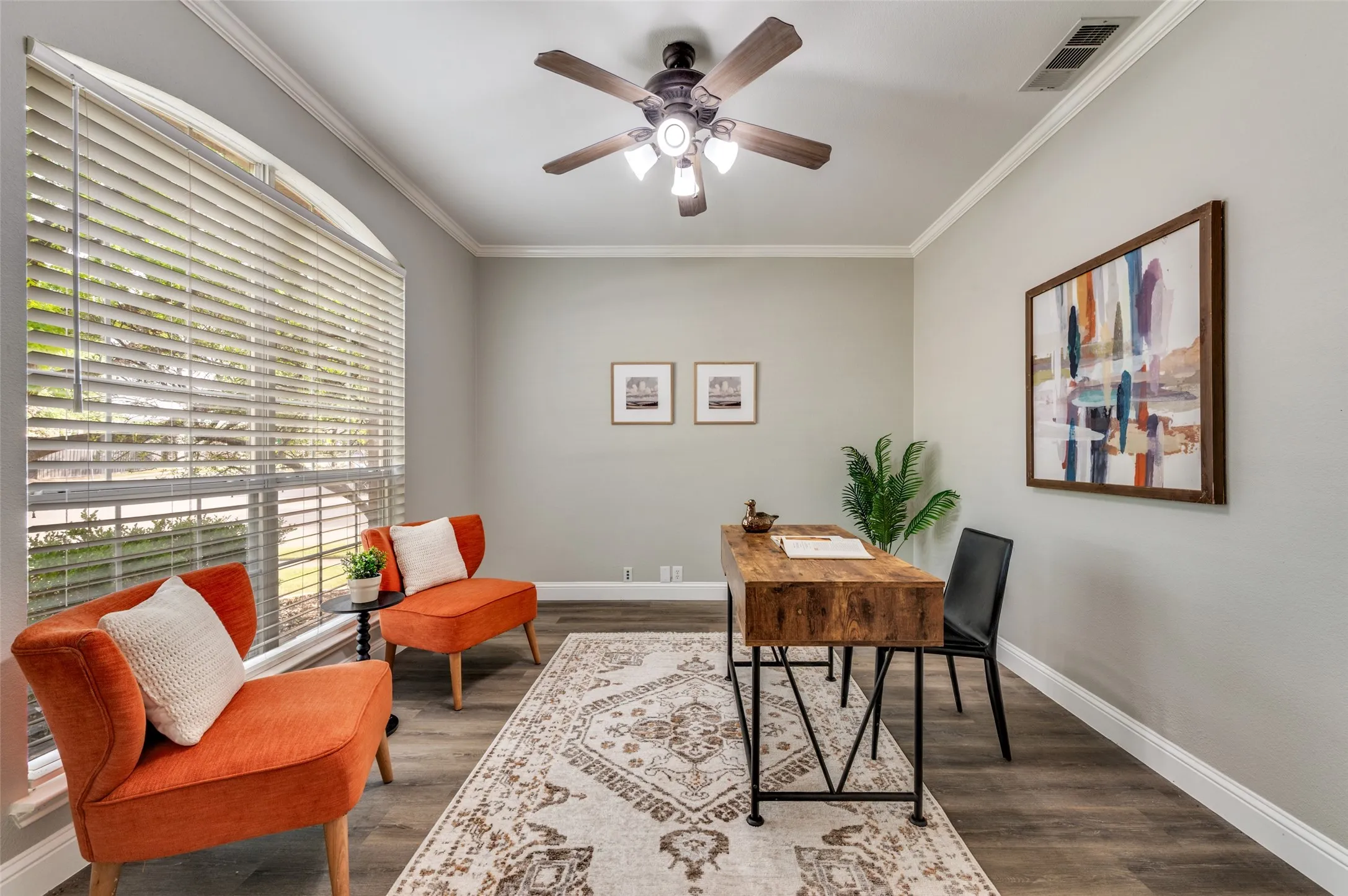 Bright home office featuring large plantation-style shutters flooding the space with natural light, wood-finish flooring, and neutral wall finishes