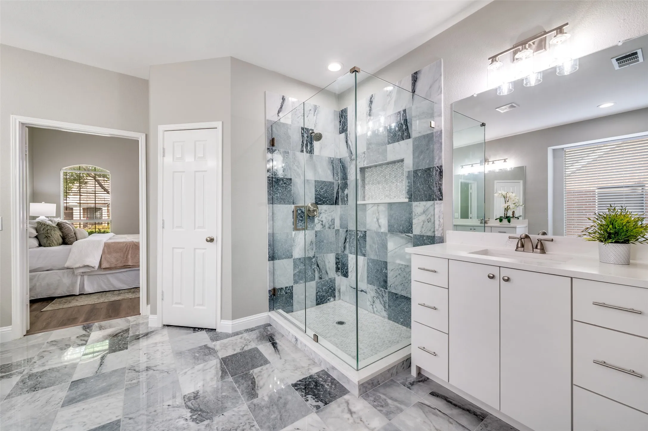 Glass-enclosed shower with tiled walls and built-in niche, dual basin vanity with white cabinetry, and large format tiled flooring