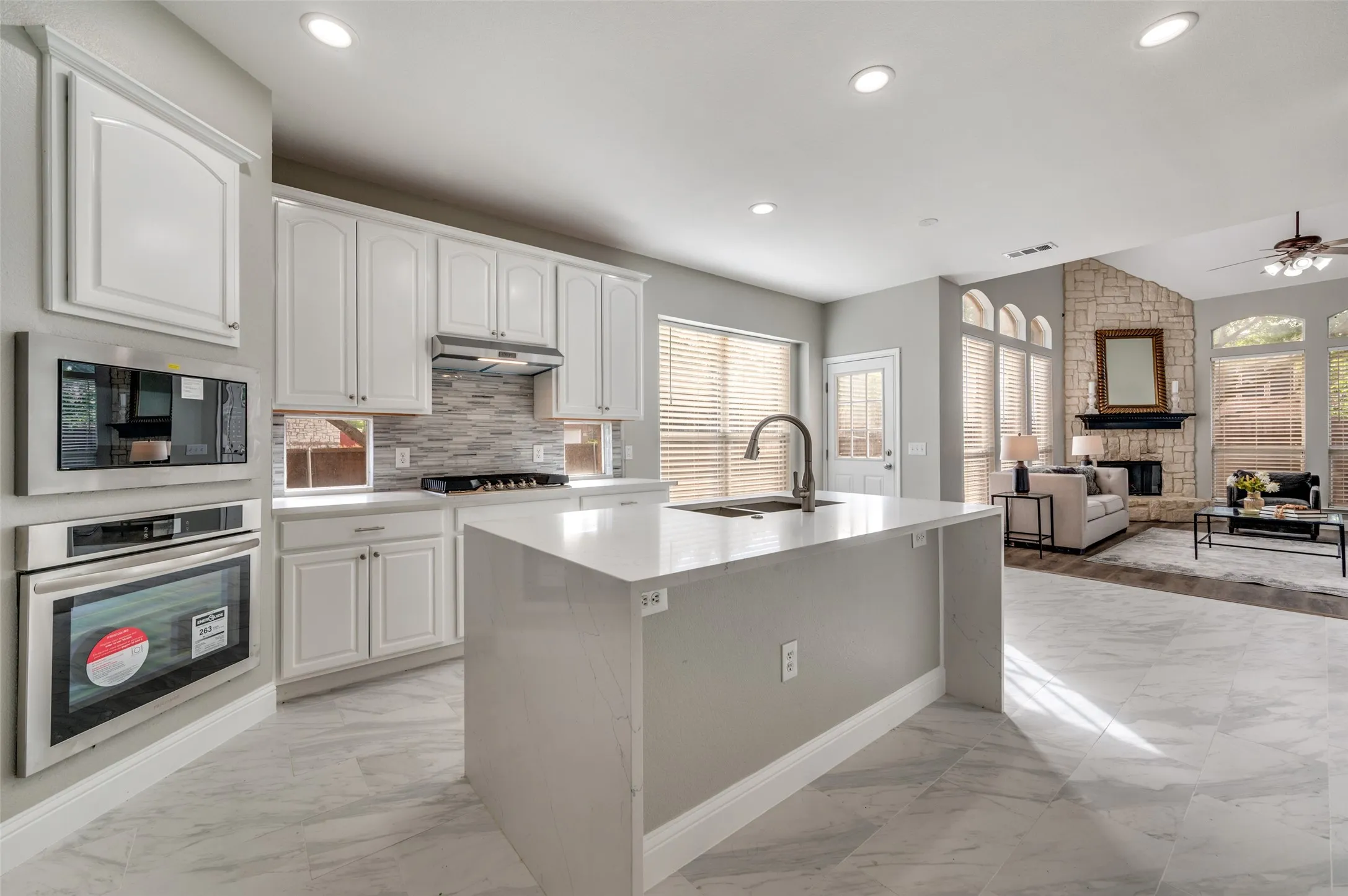 Kitchen island with integrated sink, white cabinetry, integrated stainless steel appliances, and tile flooring