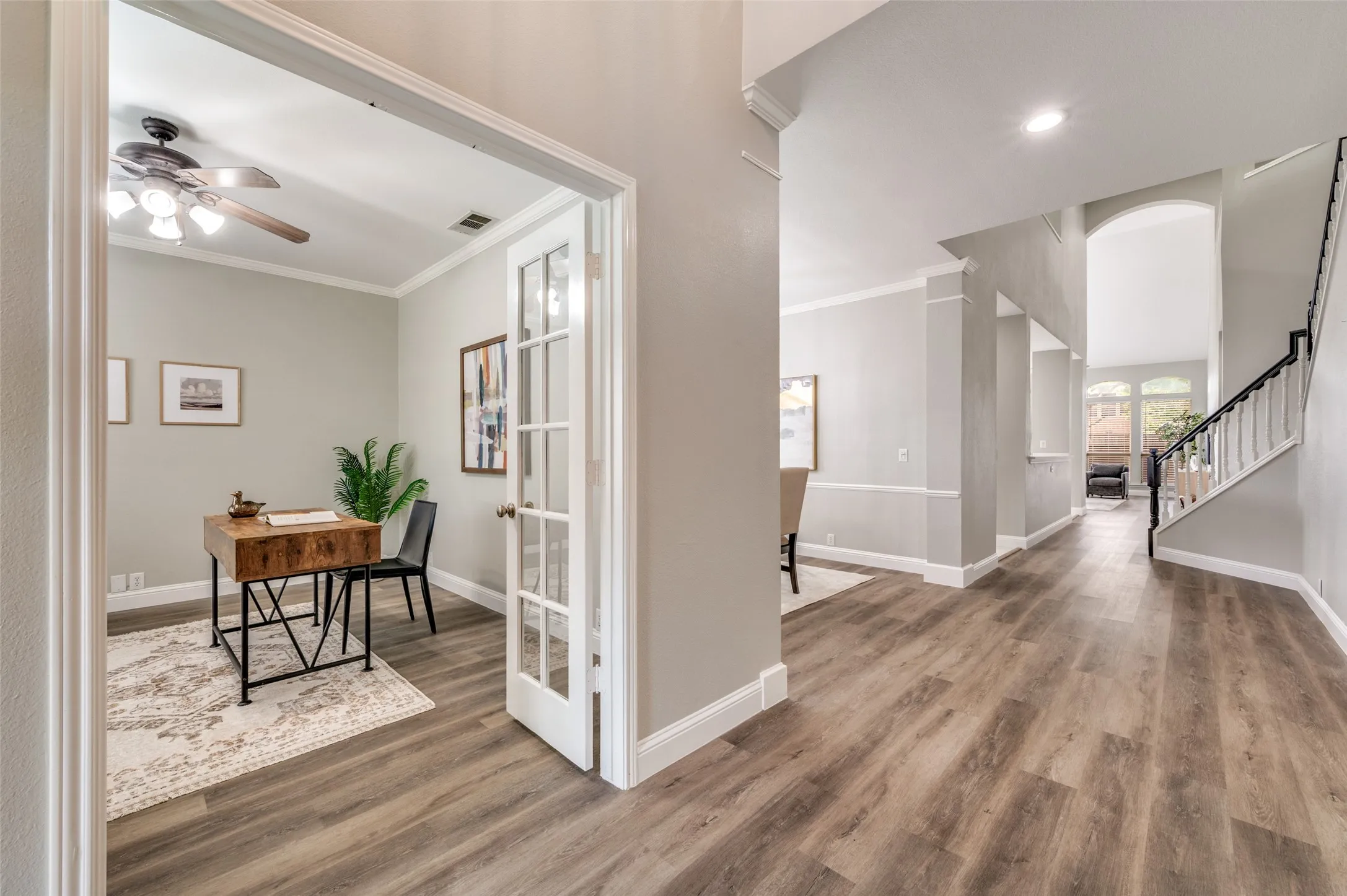 Welcoming foyer with wood-finish flooring throughout, white French doors with glass panes opening to a dedicated home office, recessed lighting, and a curved staircase with black metal railings