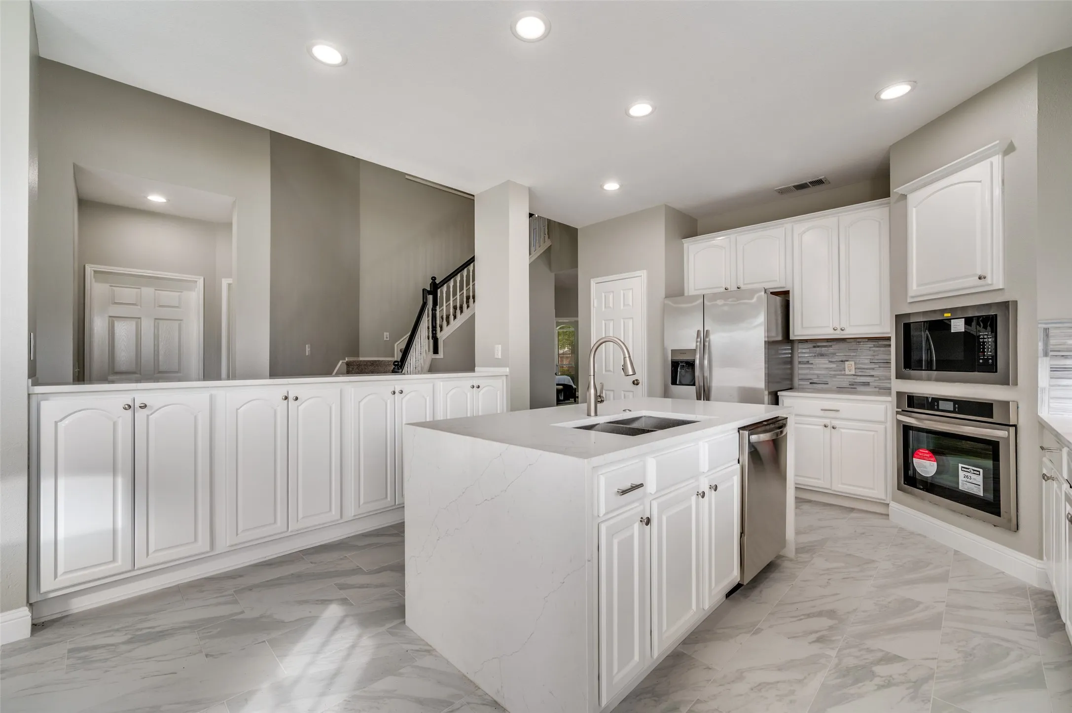 Kitchen featuring white cabinetry, stainless steel appliances, a center island with sink, and tile flooring