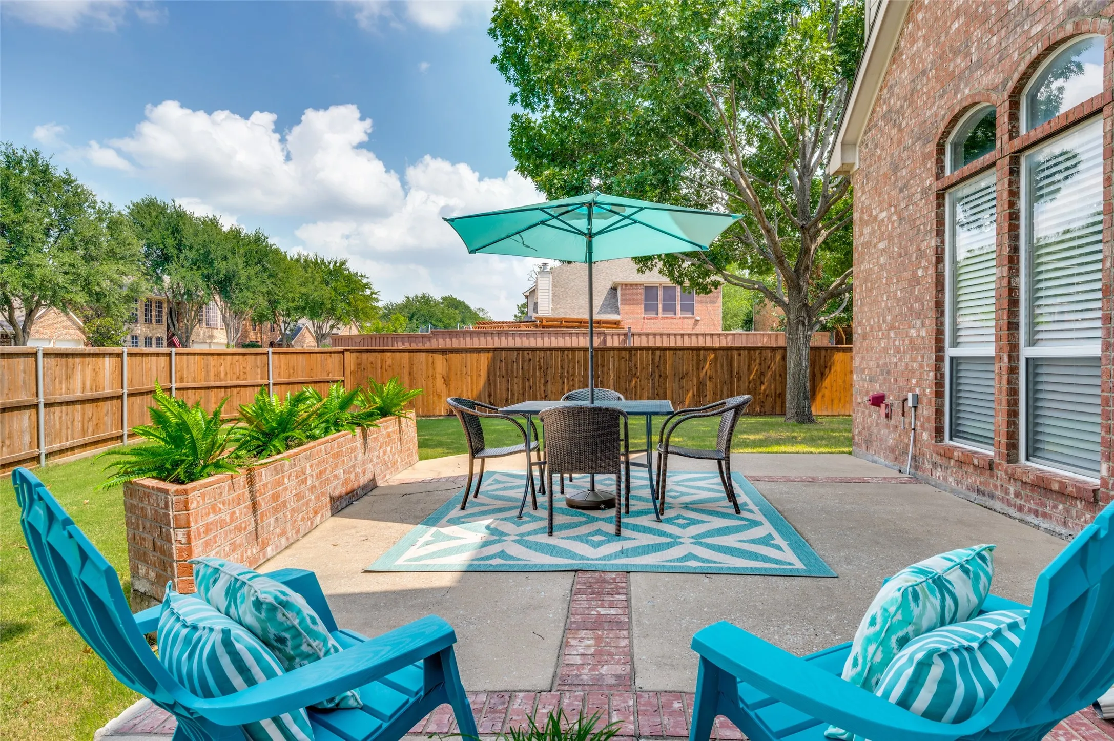 Expansive concrete patio with brick accents, featuring integrated brick planters, a manicured lawn, and a wood privacy fence