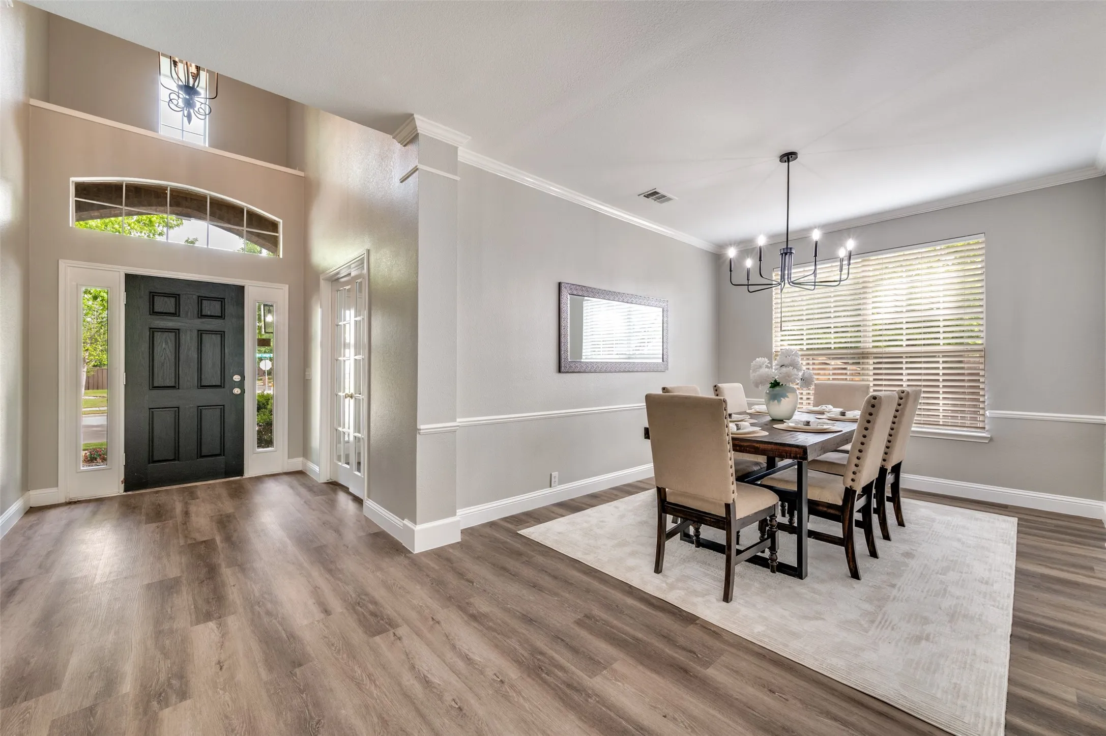 Wood-finish flooring throughout, two-story foyer with transom window, paneled front door with sidelights, crown molding, and wainscoting