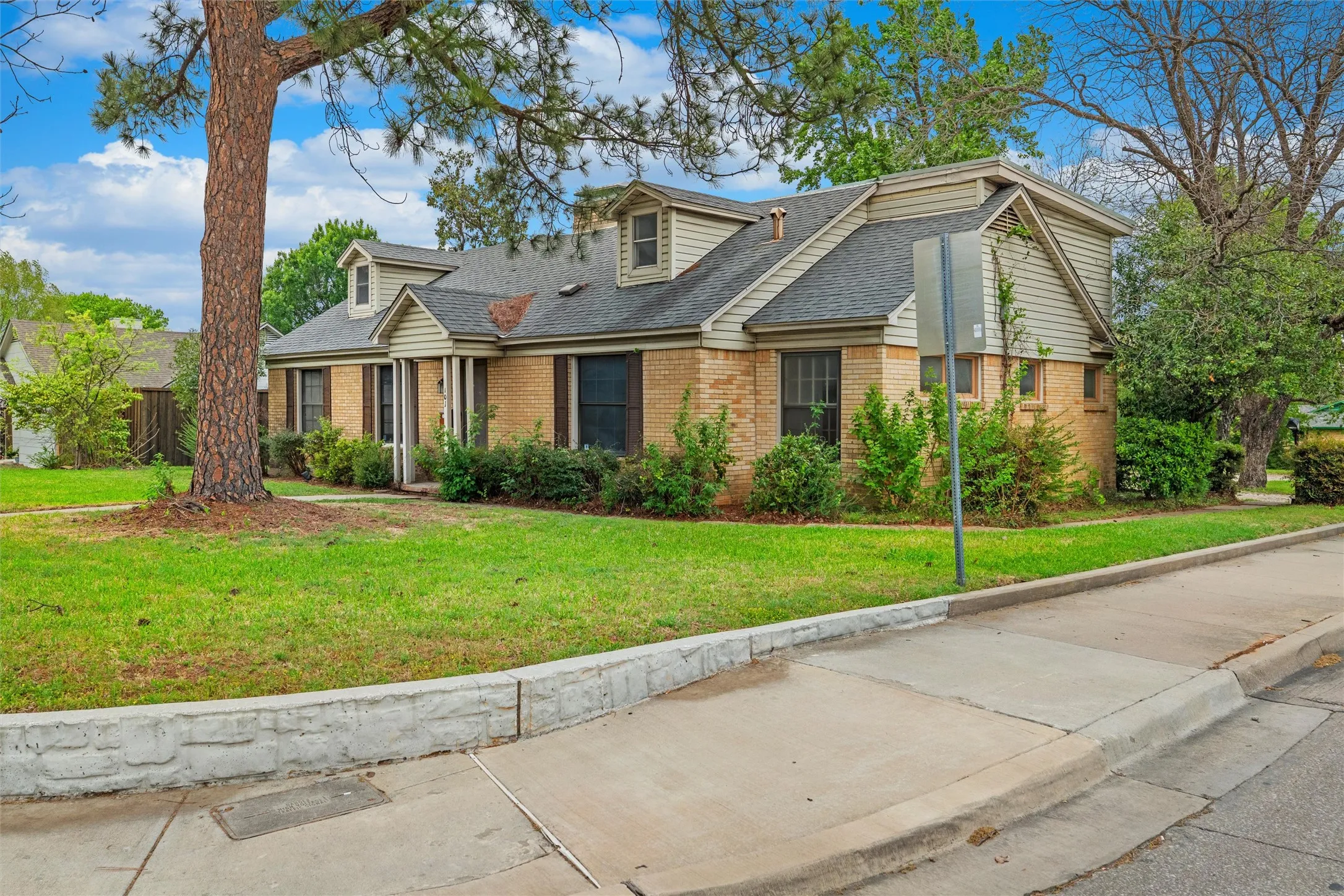 Brick and siding exterior with dormer windows, a covered entry, and established landscaping