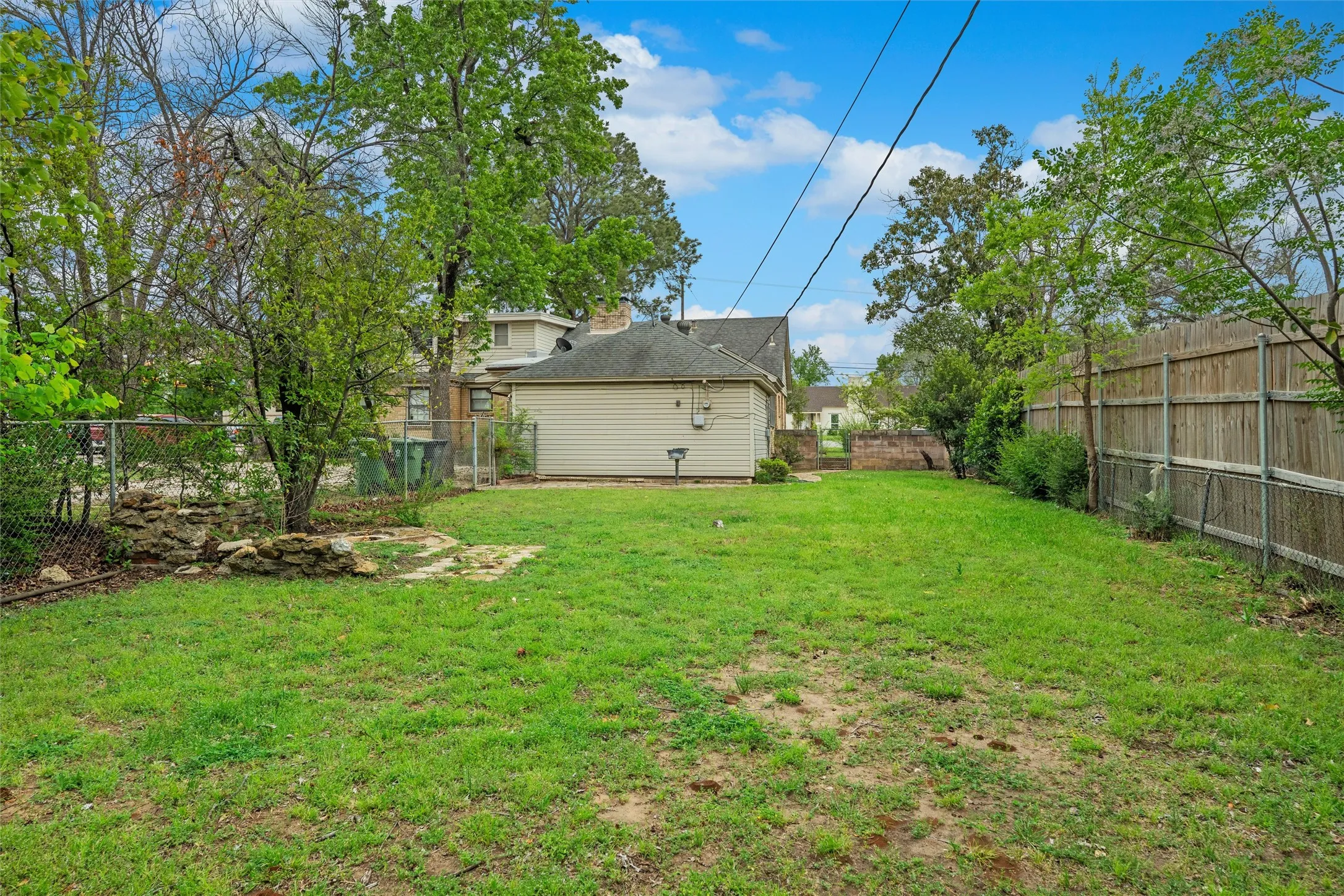 Expansive grassy yard with a chain link fence, wood panel fencing, and mature trees