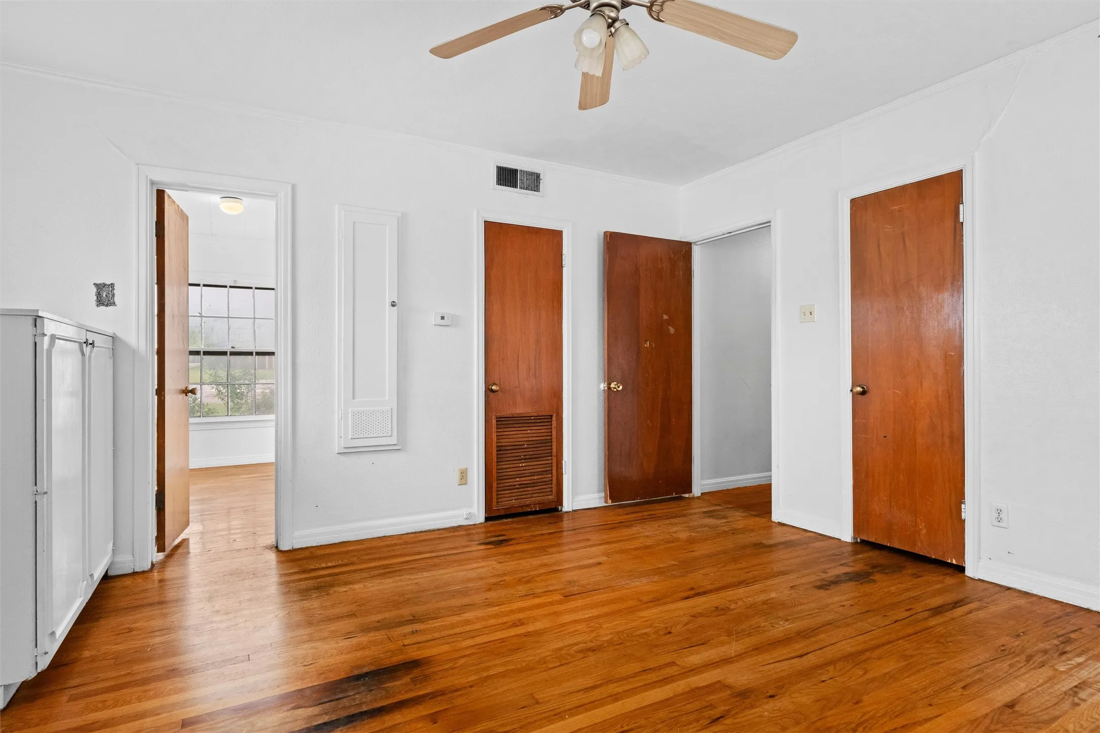 Hardwood flooring, painted white walls, ceiling fan, and multiple wood-panel doors