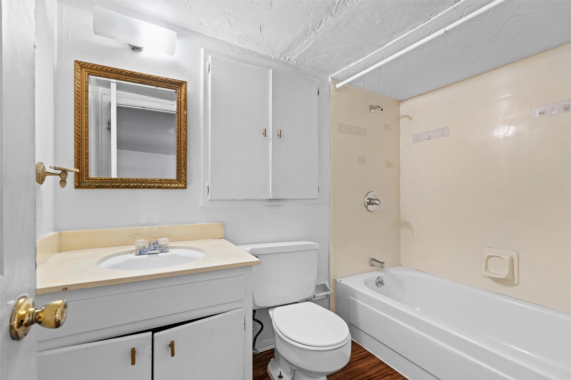 Vanity with integrated sink, gold-framed mirror, built-in storage cabinet, white toilet, and tub with shower
