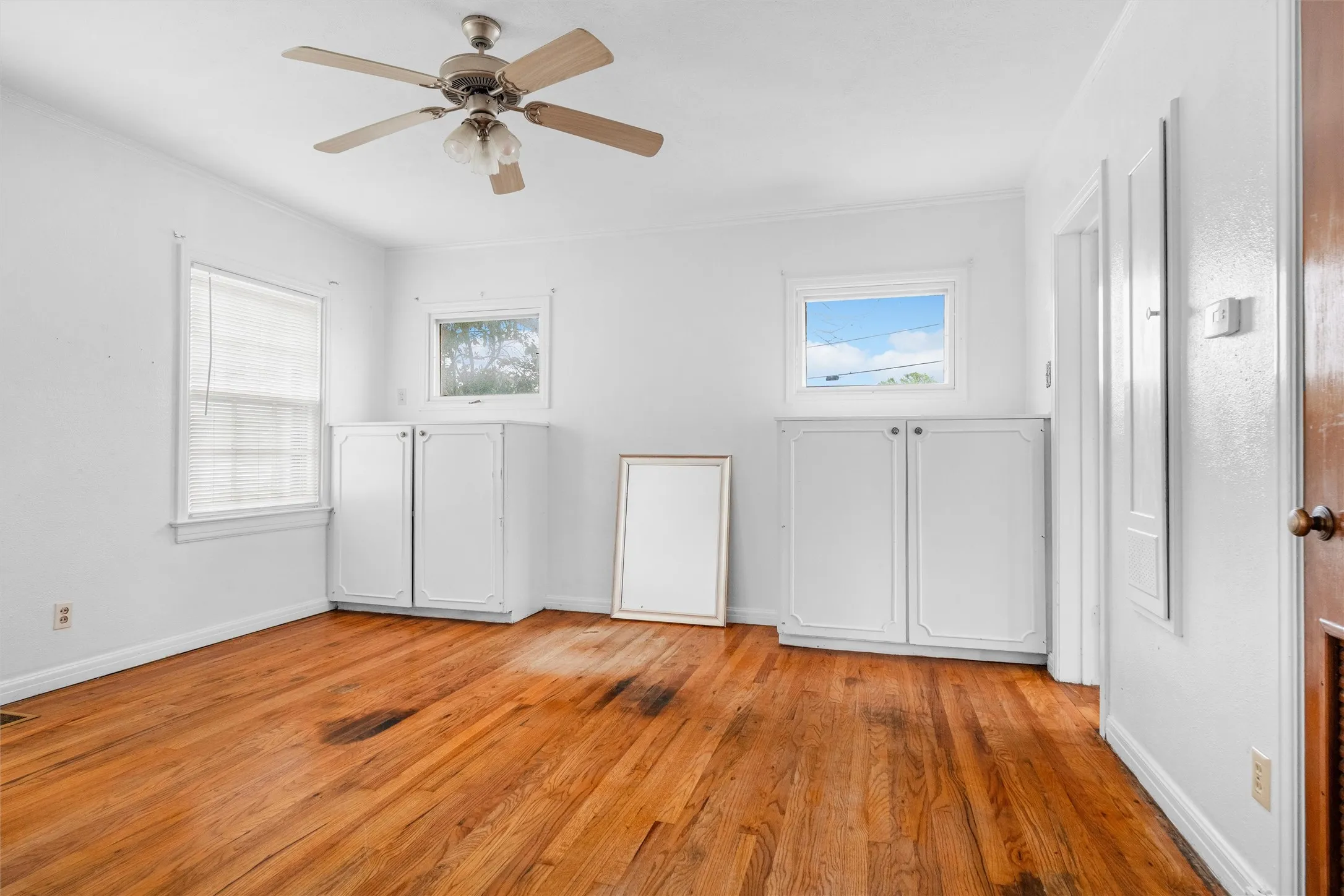Hardwood flooring, two windows, two built-in cabinets, and a ceiling fan with integrated lighting