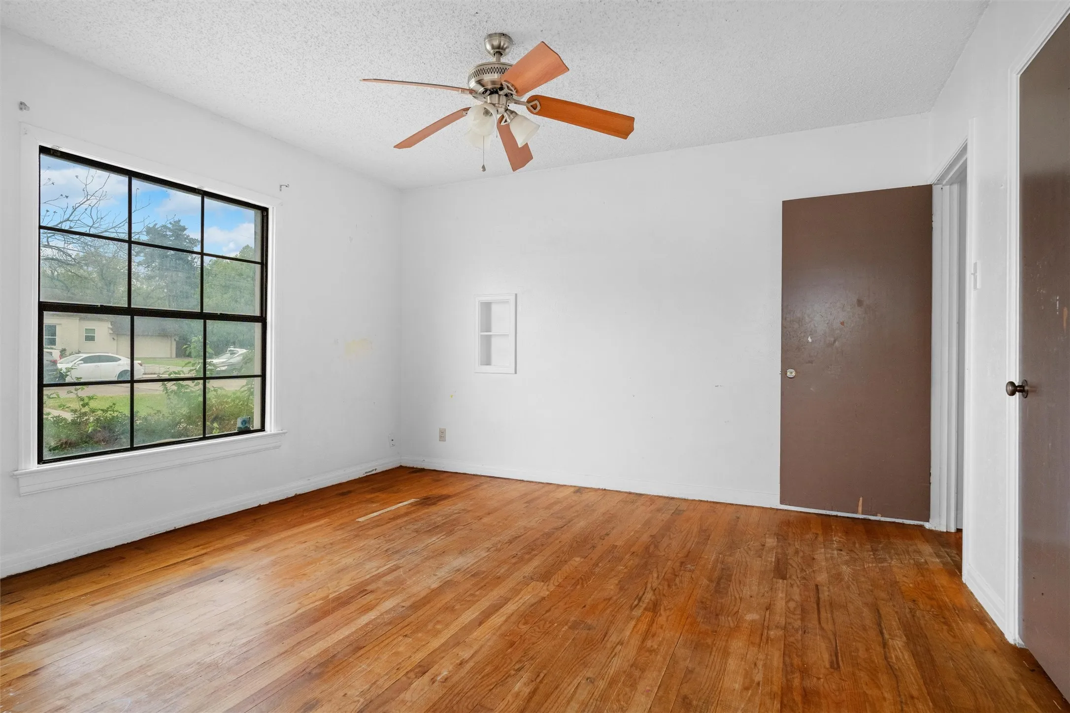 Wood-finish flooring, ceiling fan, built-in wall niche, multiple doors, and a large window