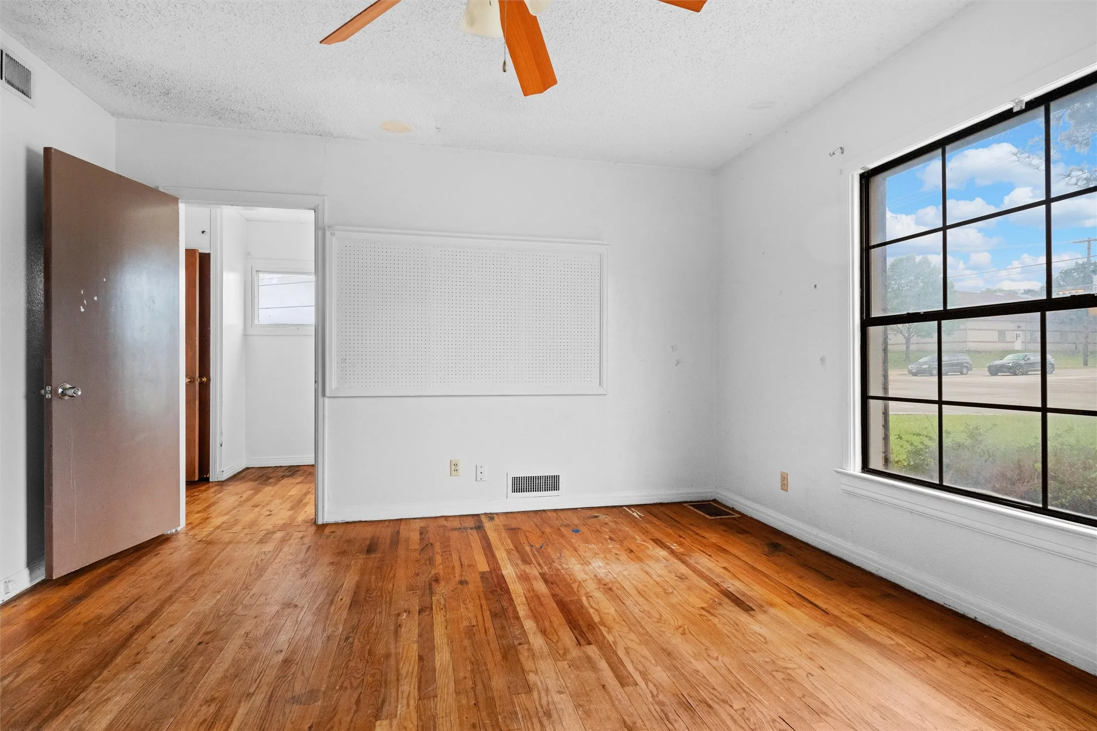 Wood-finish flooring, white walls, and a multi-pane window with black trim