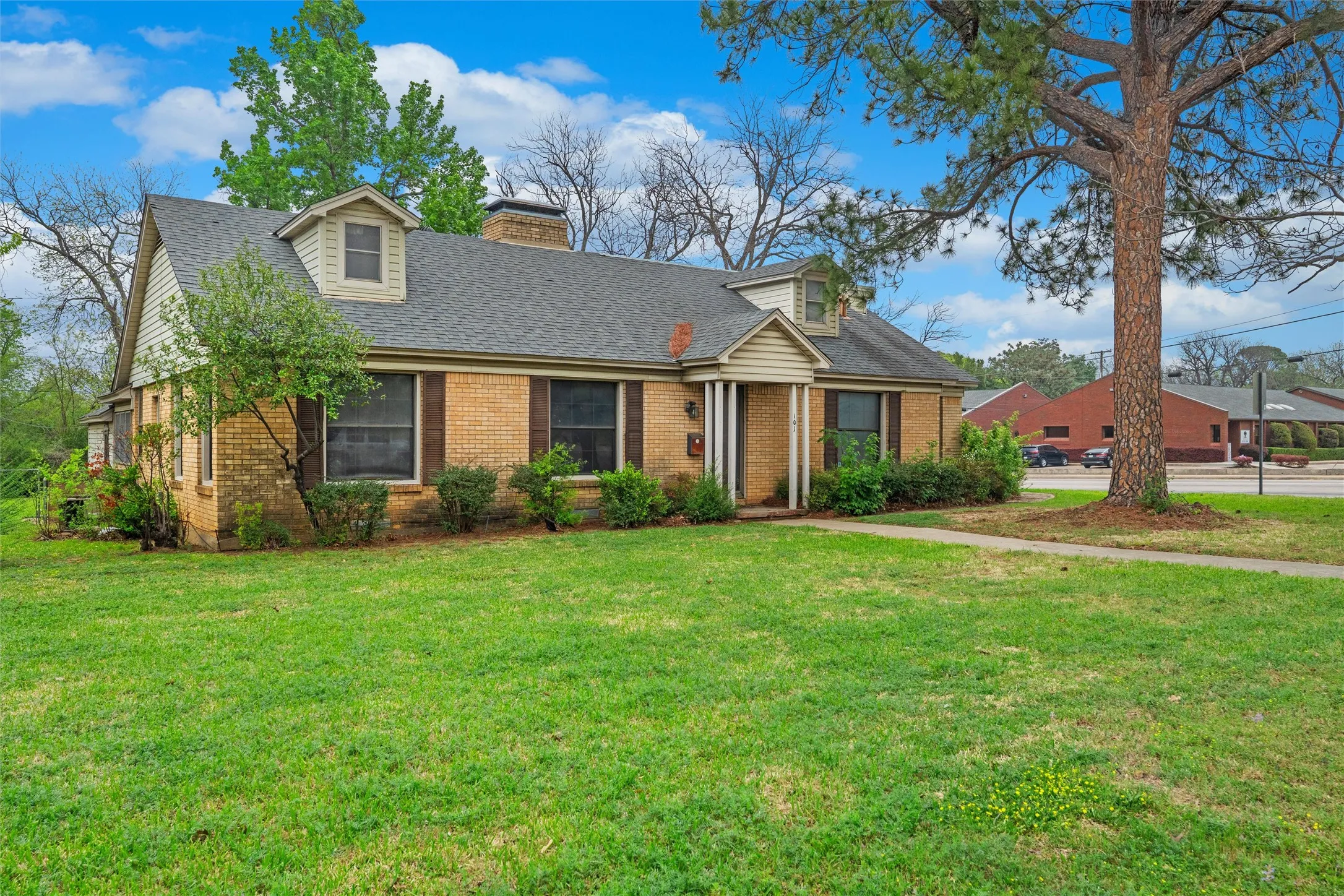 Brick exterior with dormer windows, a covered front entry, and a mature tree in the front yard