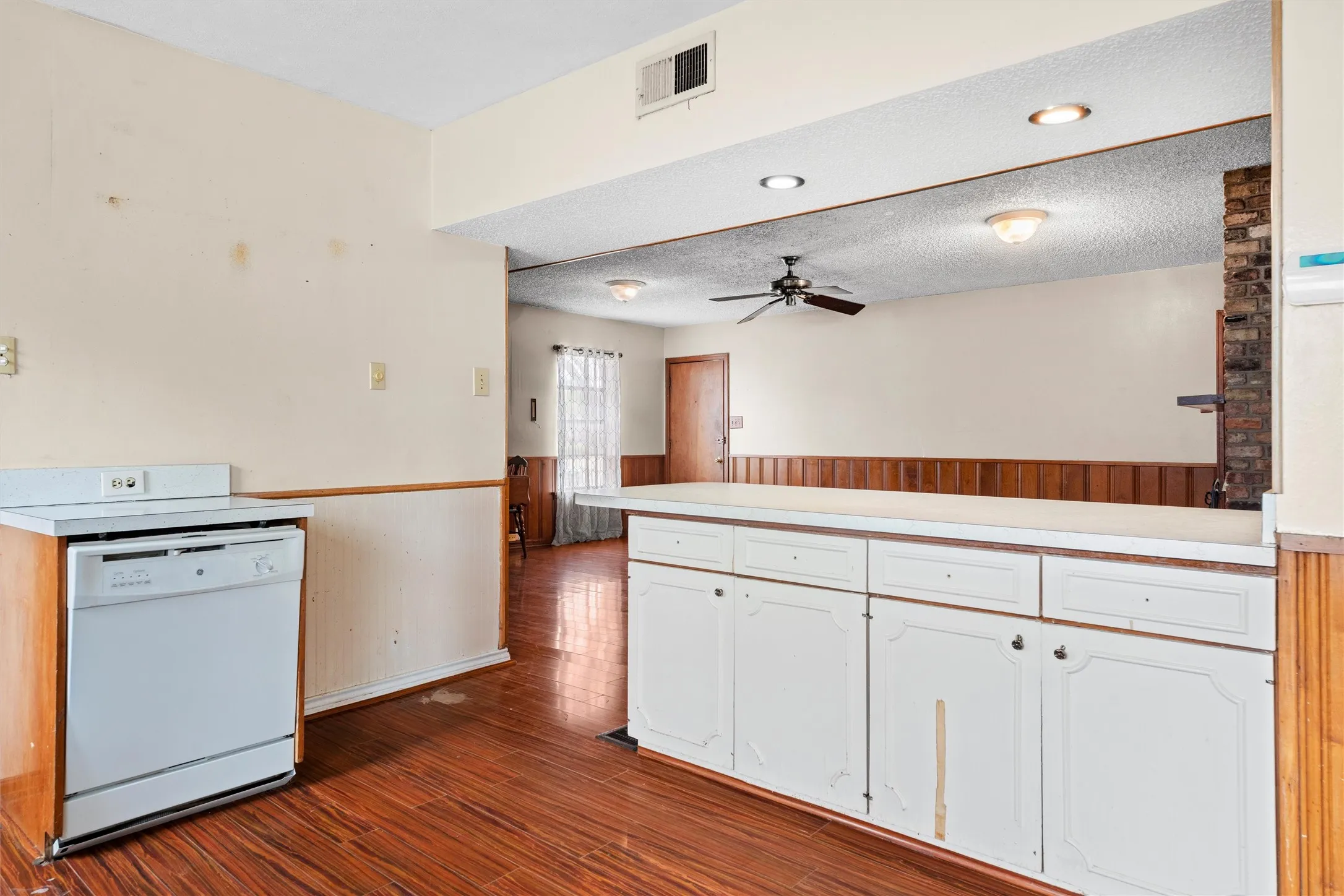 Wood-finish flooring with white base cabinetry, white countertop, and wood-paneled accents