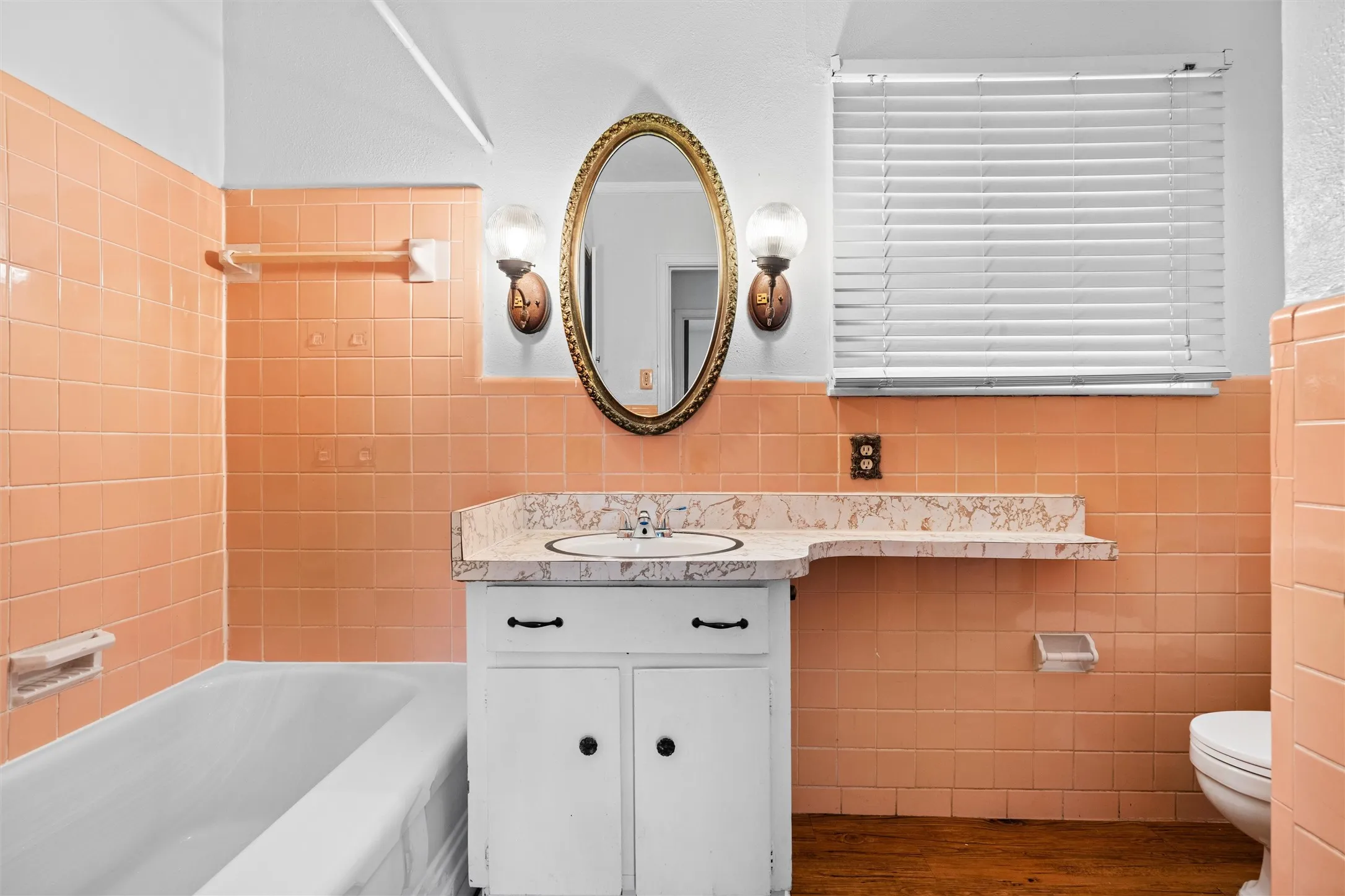 Bathroom featuring floor-to-ceiling peach wall tile, a white vanity with an integrated sink, and an oval mirror with dual sconces