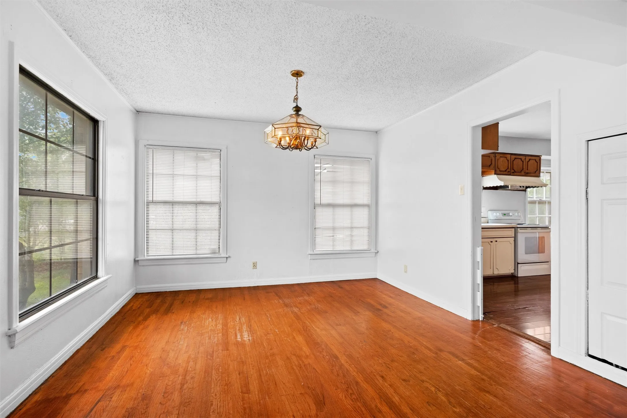 Warm wood flooring, multiple windows providing natural illumination, and a classic chandelier