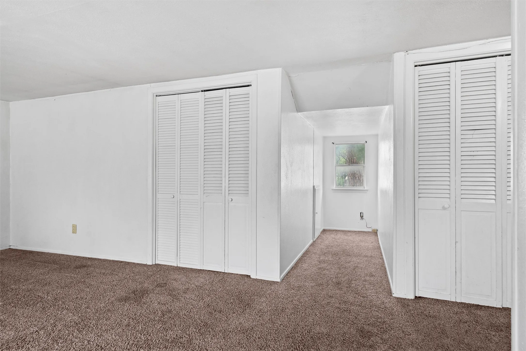 Brown carpet flooring, white painted walls, louvered bi-fold closet doors, and a single-pane window