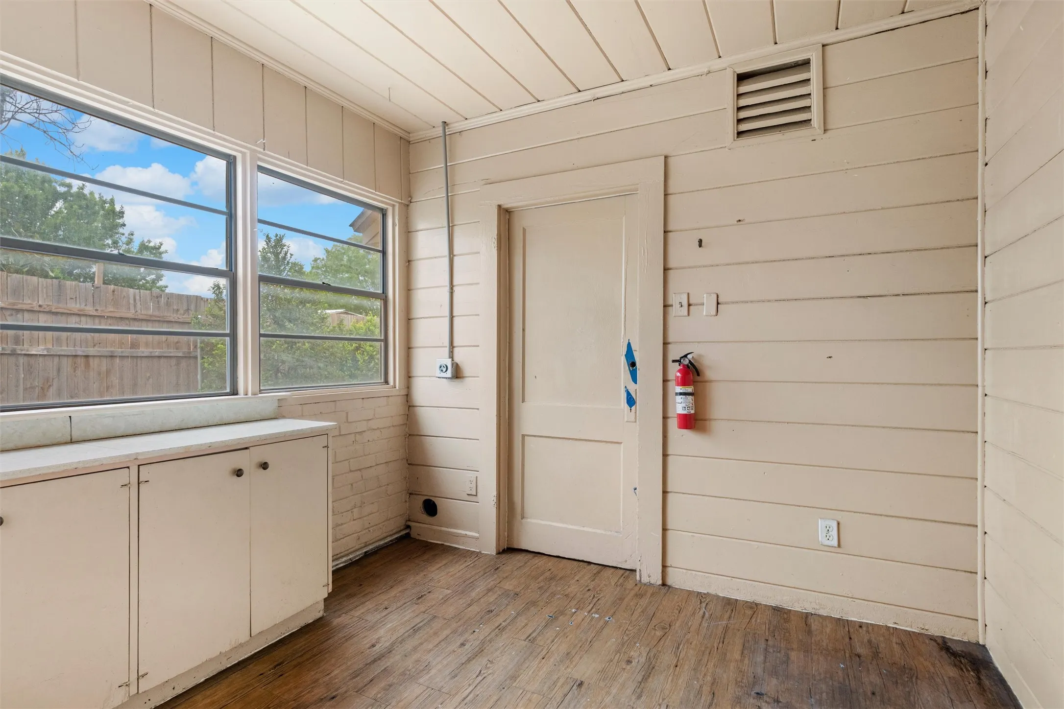Multiple windows providing natural light, wood-finish flooring, white built-in cabinetry with dark hardware, plank wall paneling, and an interior door