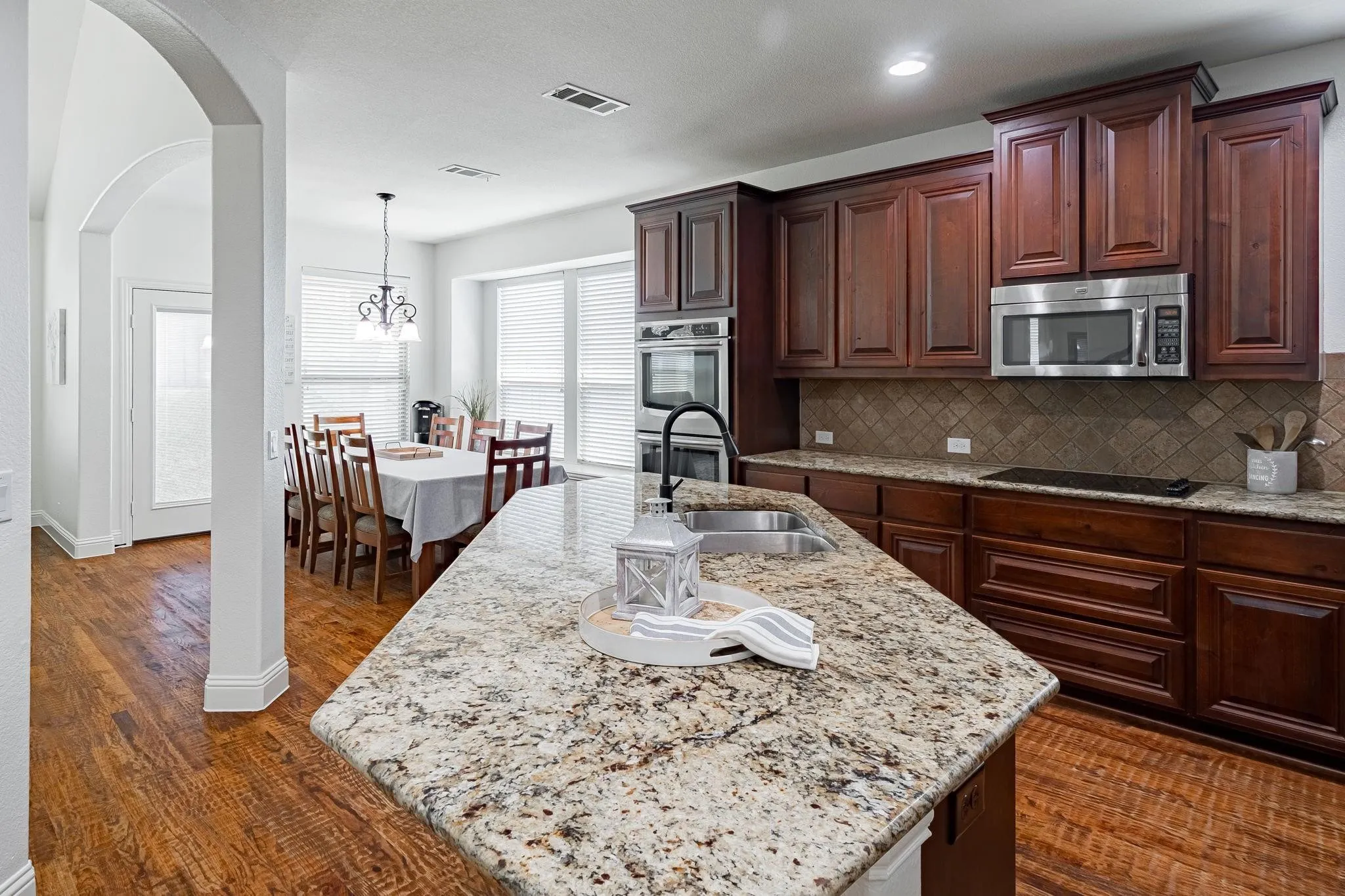 Kitchen featuring wood-finish flooring, dark wood cabinetry, granite countertops, and stainless steel appliances