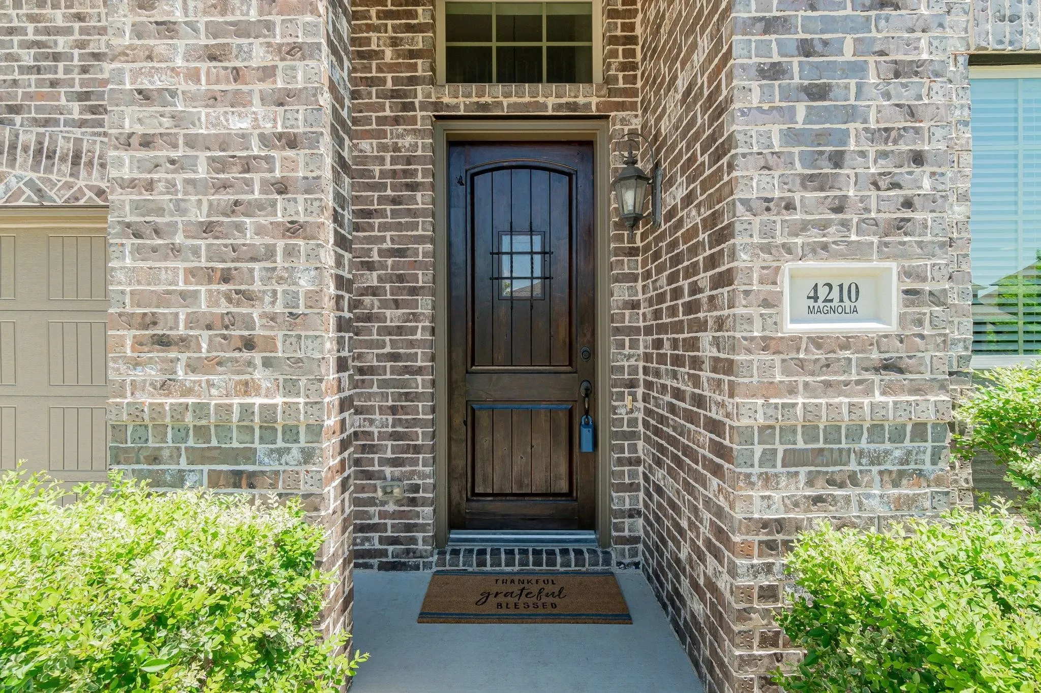 Brick exterior with an arched entryway, featuring a dark wood door with glass inserts and an exterior wall lantern