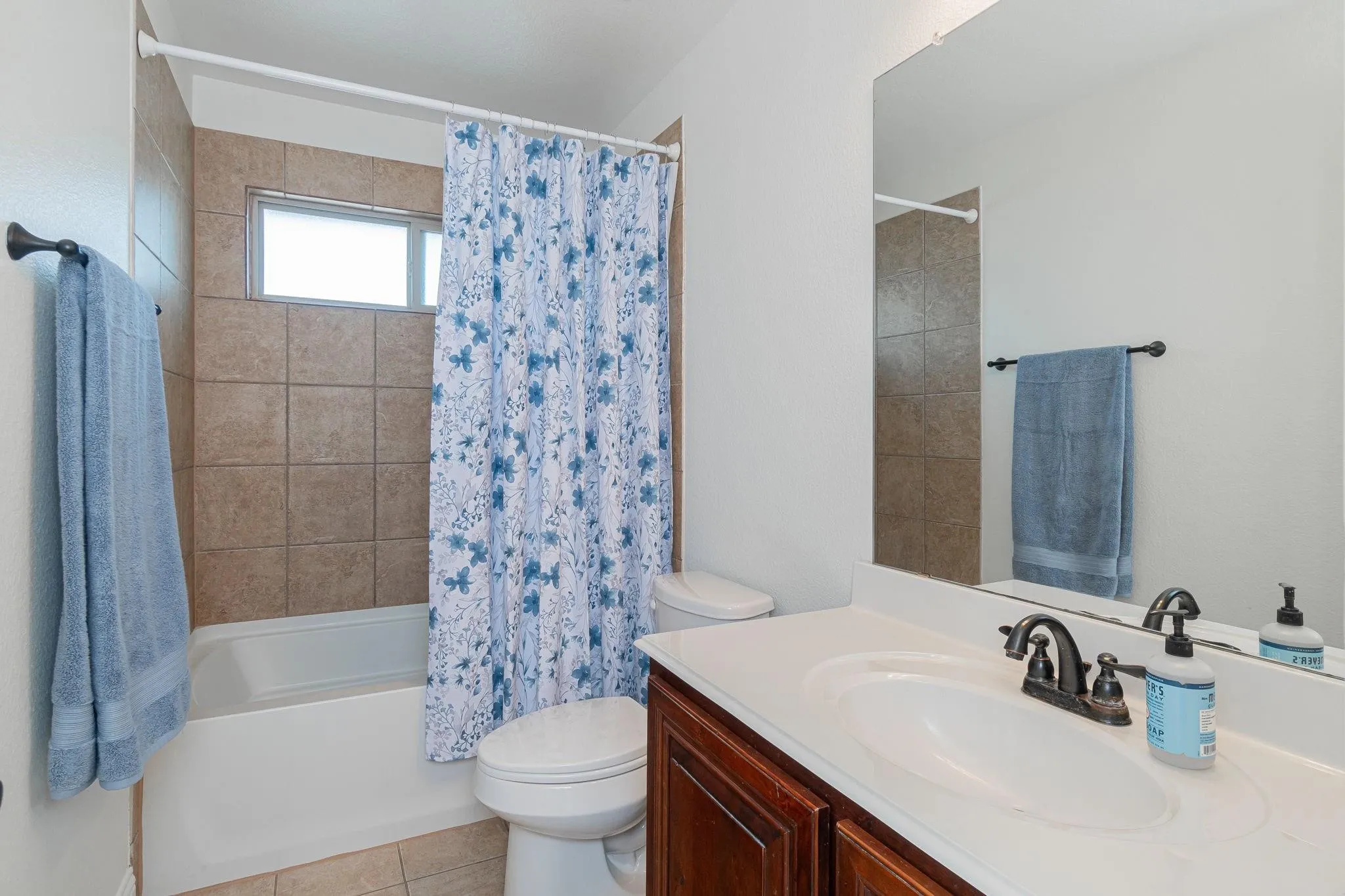 Bathroom featuring a white vanity with an integrated sink, dark wood-finish cabinetry, a full-width wall mirror, and a tub/shower combination with tiled surround