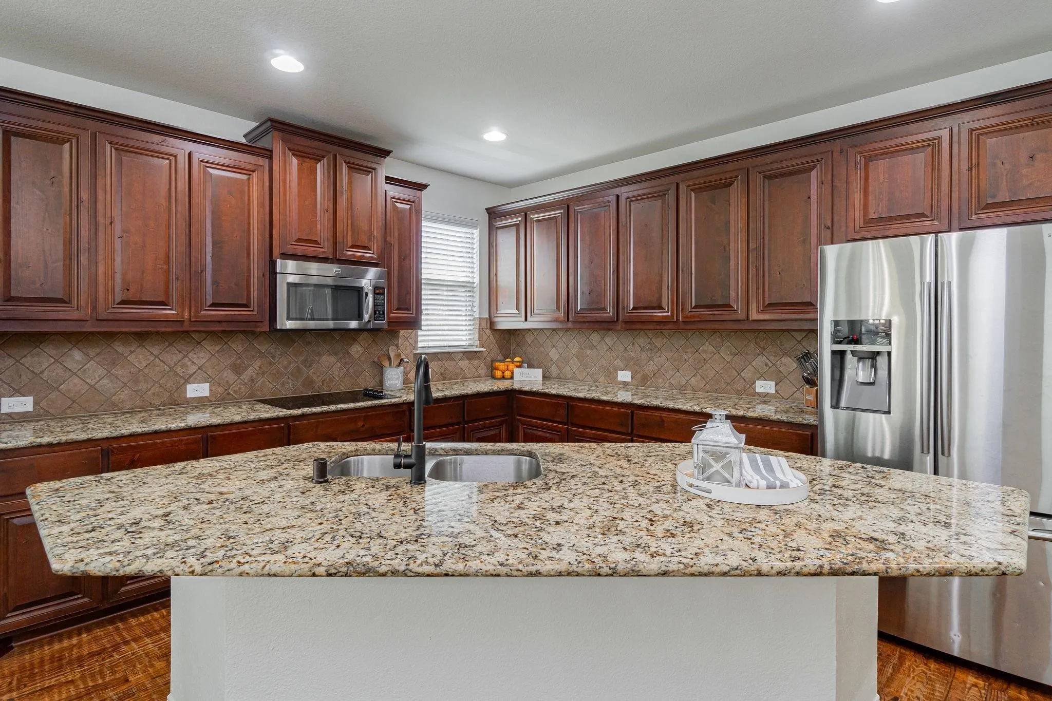 Kitchen featuring a large island with a double basin sink, stainless steel appliances, wood-finish cabinetry, and tiled backsplash