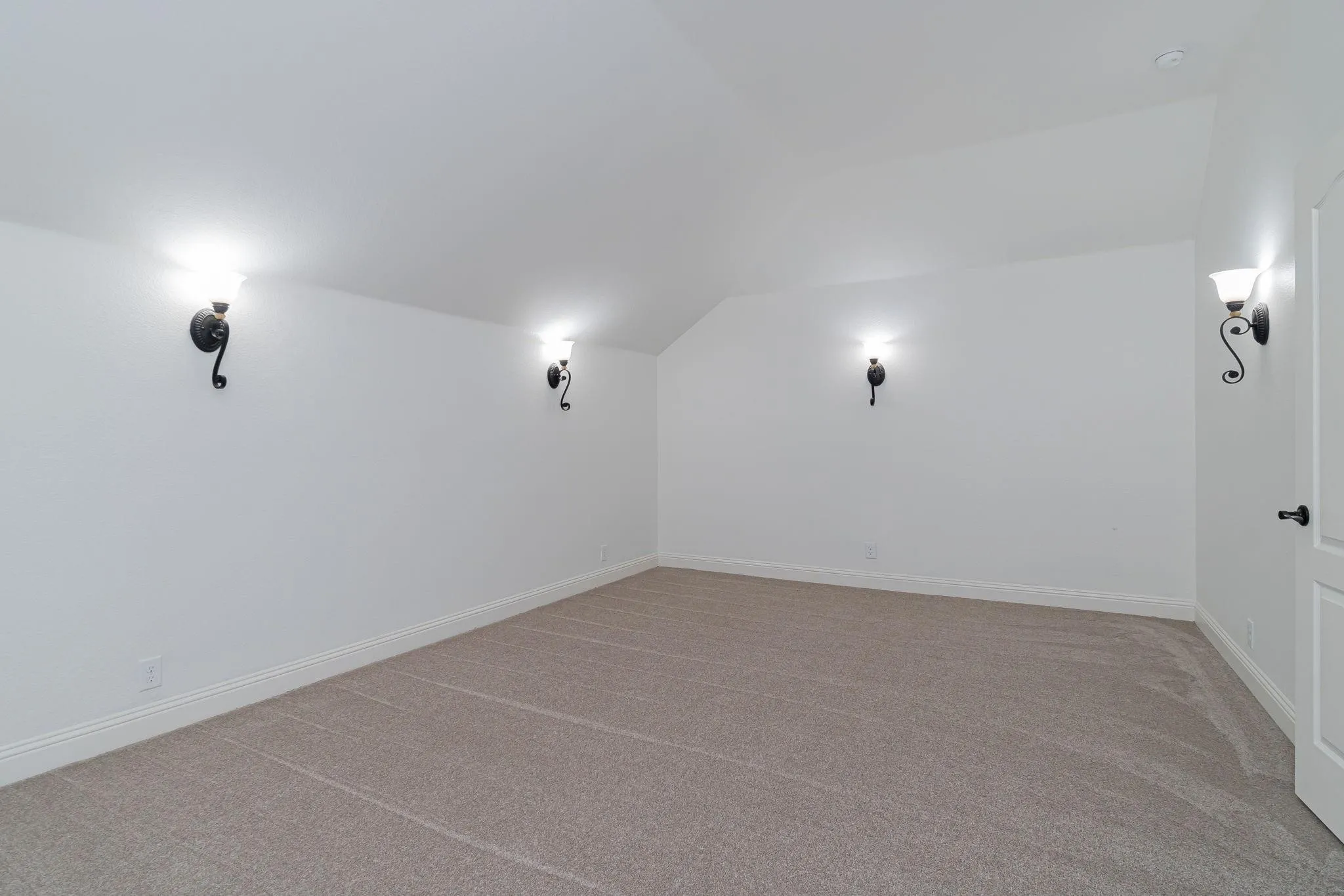 Sloped ceiling room featuring carpet flooring, crisp white walls, and decorative wall sconces