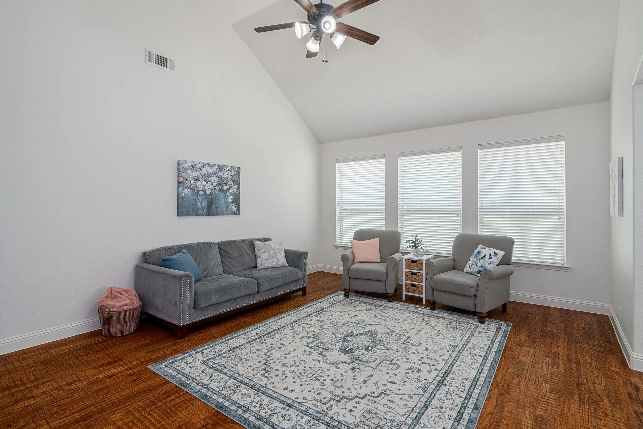 Vaulted ceilings with a ceiling fan, three windows with blinds, and wood-finish flooring