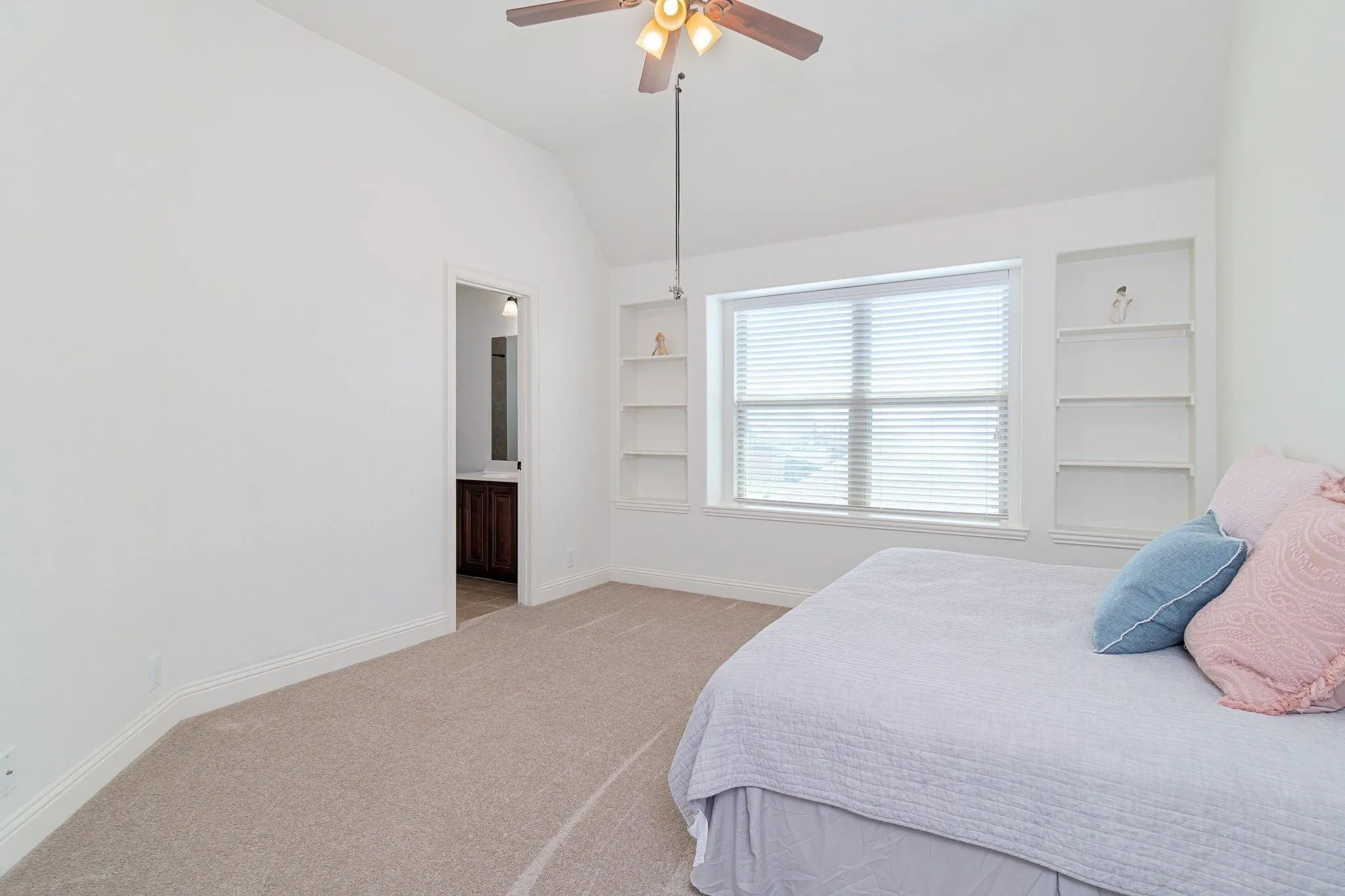 Vaulted ceiling, built-in shelving, ceiling fan with light fixture, window with blinds, and neutral carpet flooring