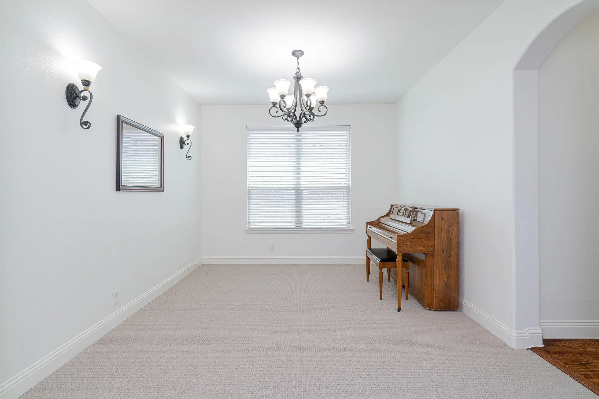 Recessed window with blinds, wrought iron chandelier, wall sconces, arched doorway, and carpeted flooring