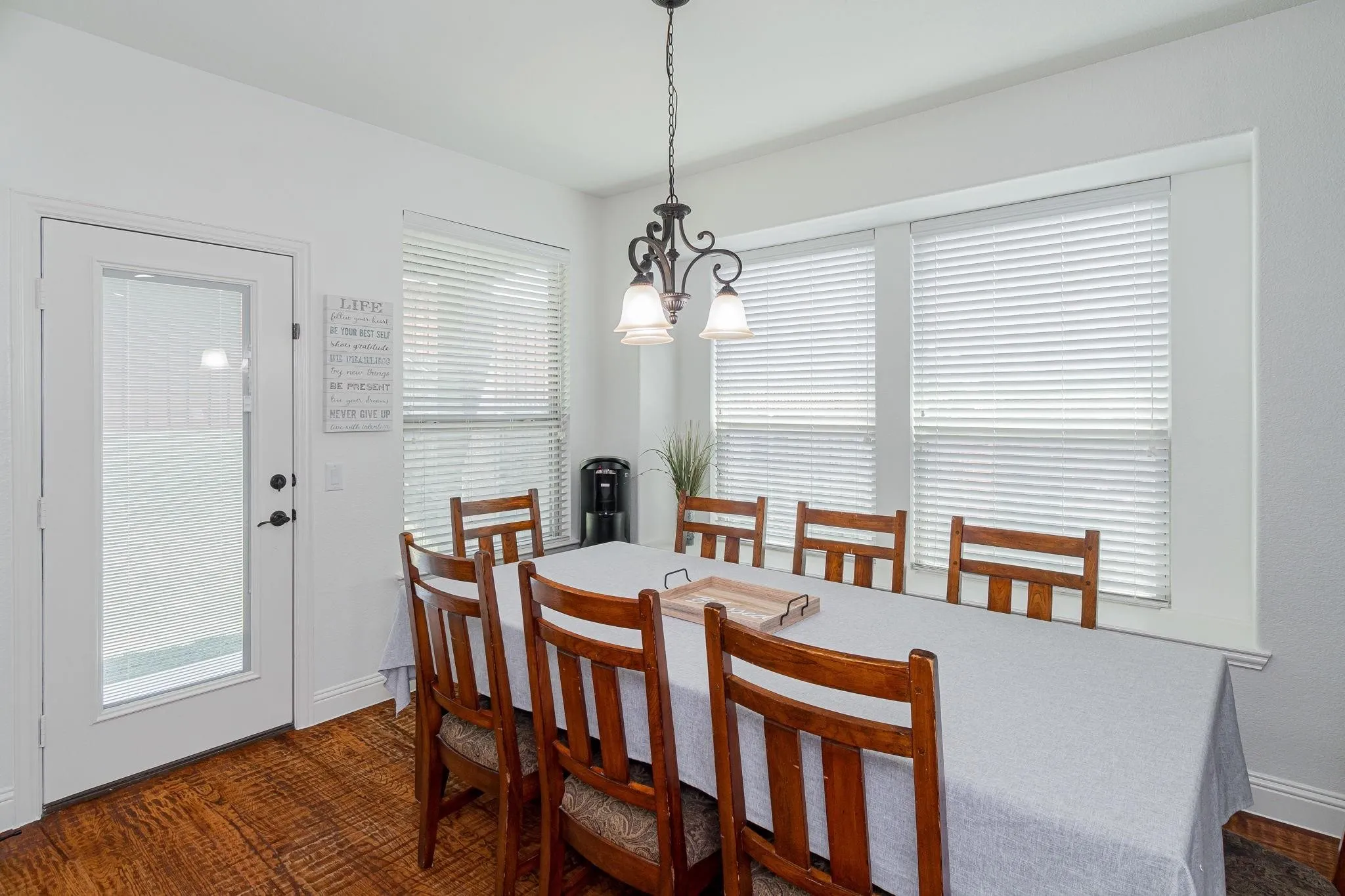 Wood-finish flooring, white walls, white trim, glass-paneled door, and a multi-pane window with white blinds