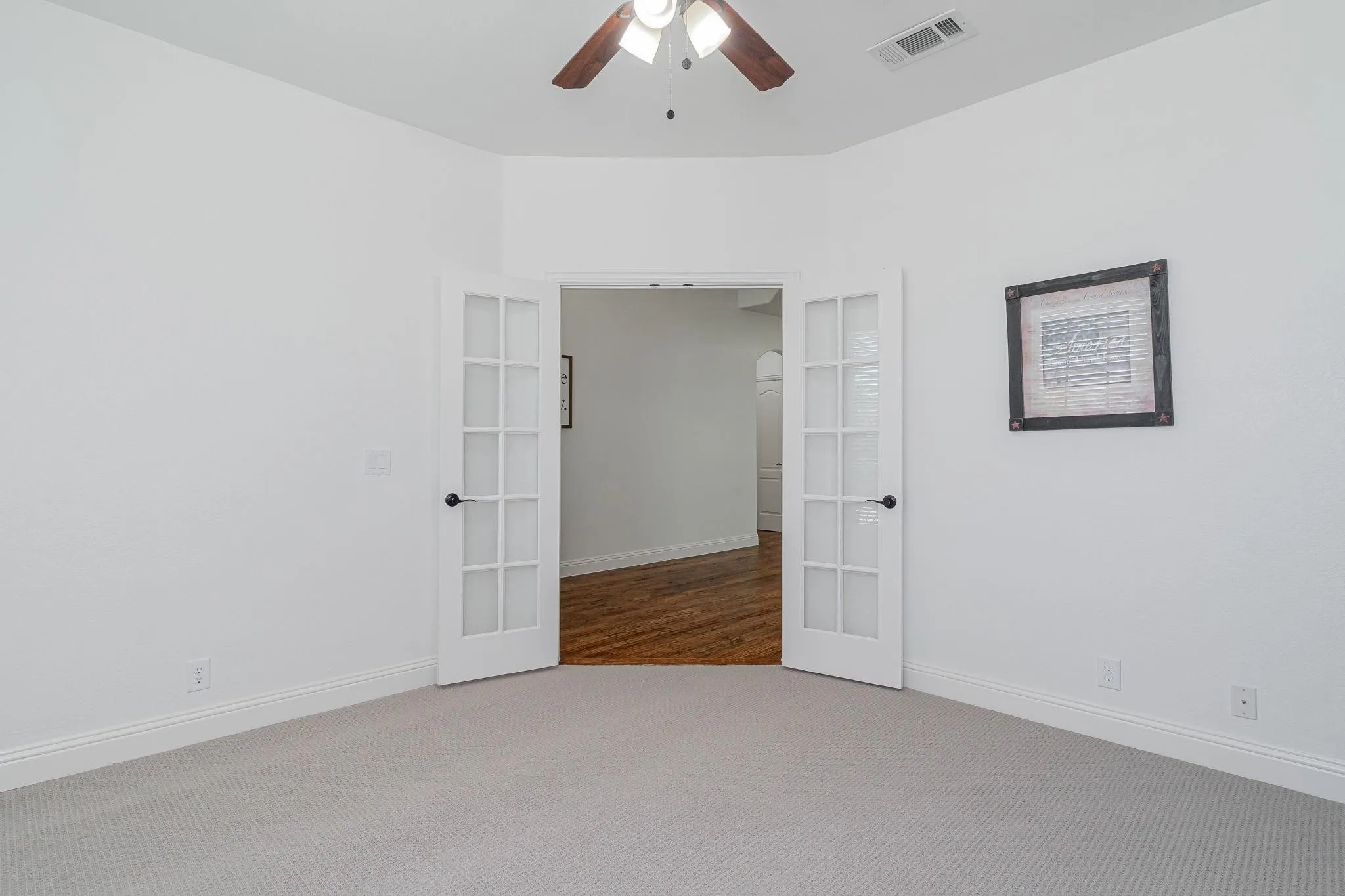 Light-colored carpeting with white baseboards, a ceiling fan with light fixture, and French doors