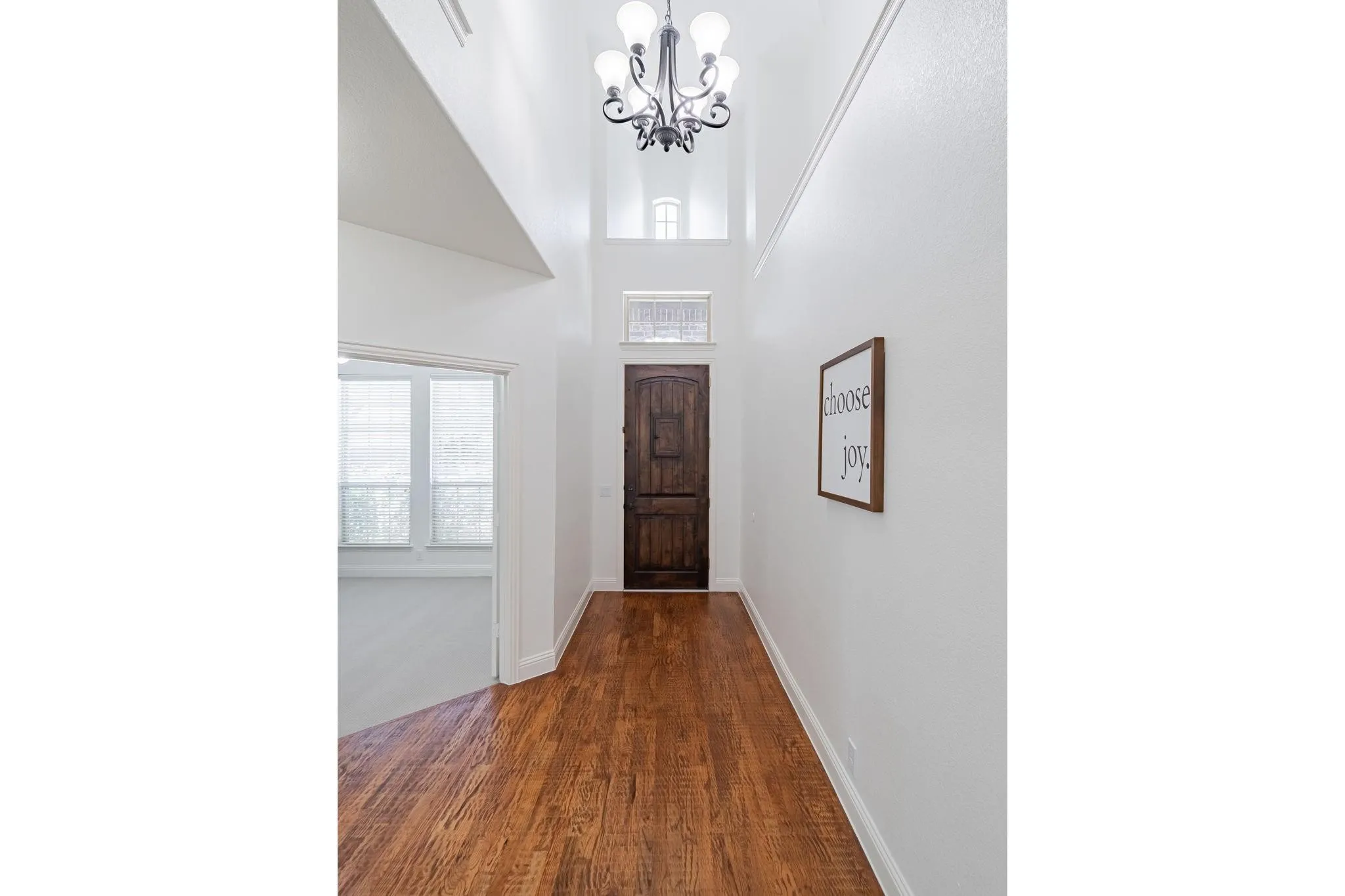 Vaulted entryway featuring a decorative chandelier, rich wood-finish flooring, and a carved wood entry door with transom window