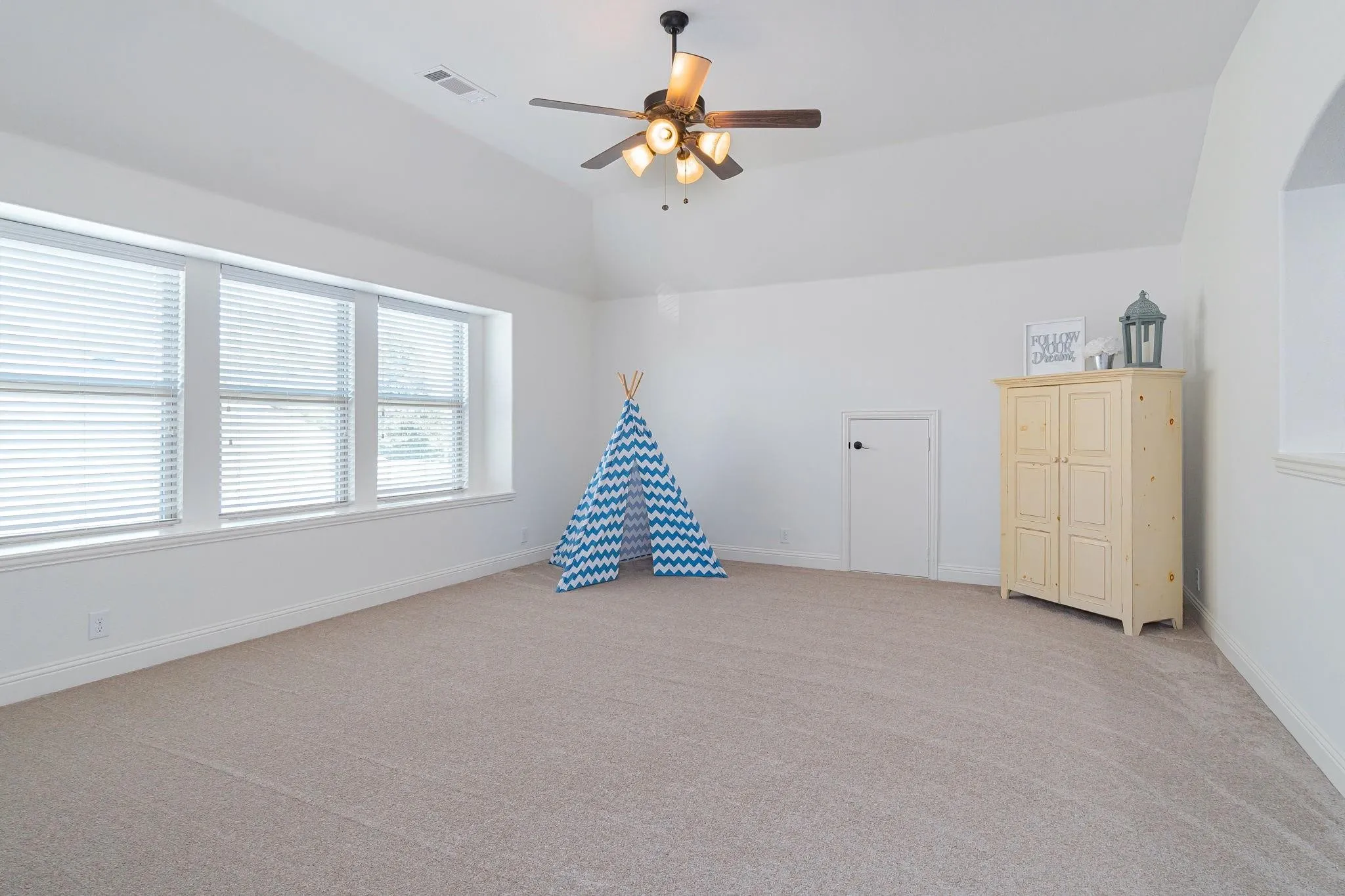 Vaulted ceiling with a ceiling fan, carpeted flooring, multiple windows, and a built-in arched alcove