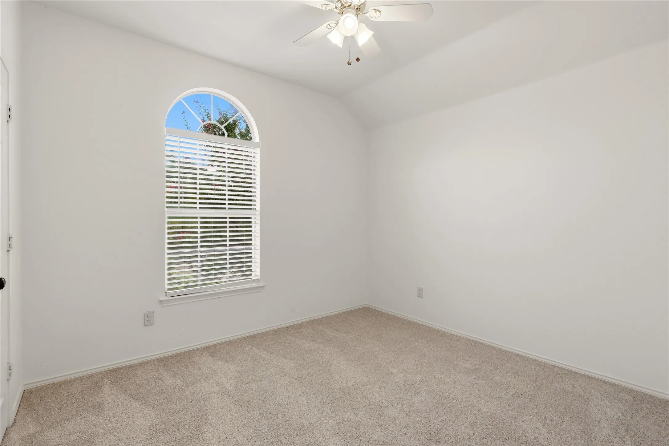 Vaulted ceiling, arched window, ceiling fan with integrated lighting, wall-to-wall carpeting, and white walls