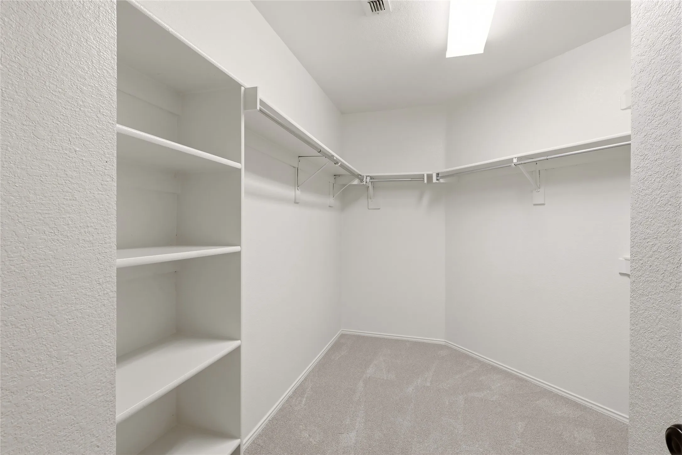 Walk-in closet featuring white shelving, multiple hanging rods, and light-toned carpeting