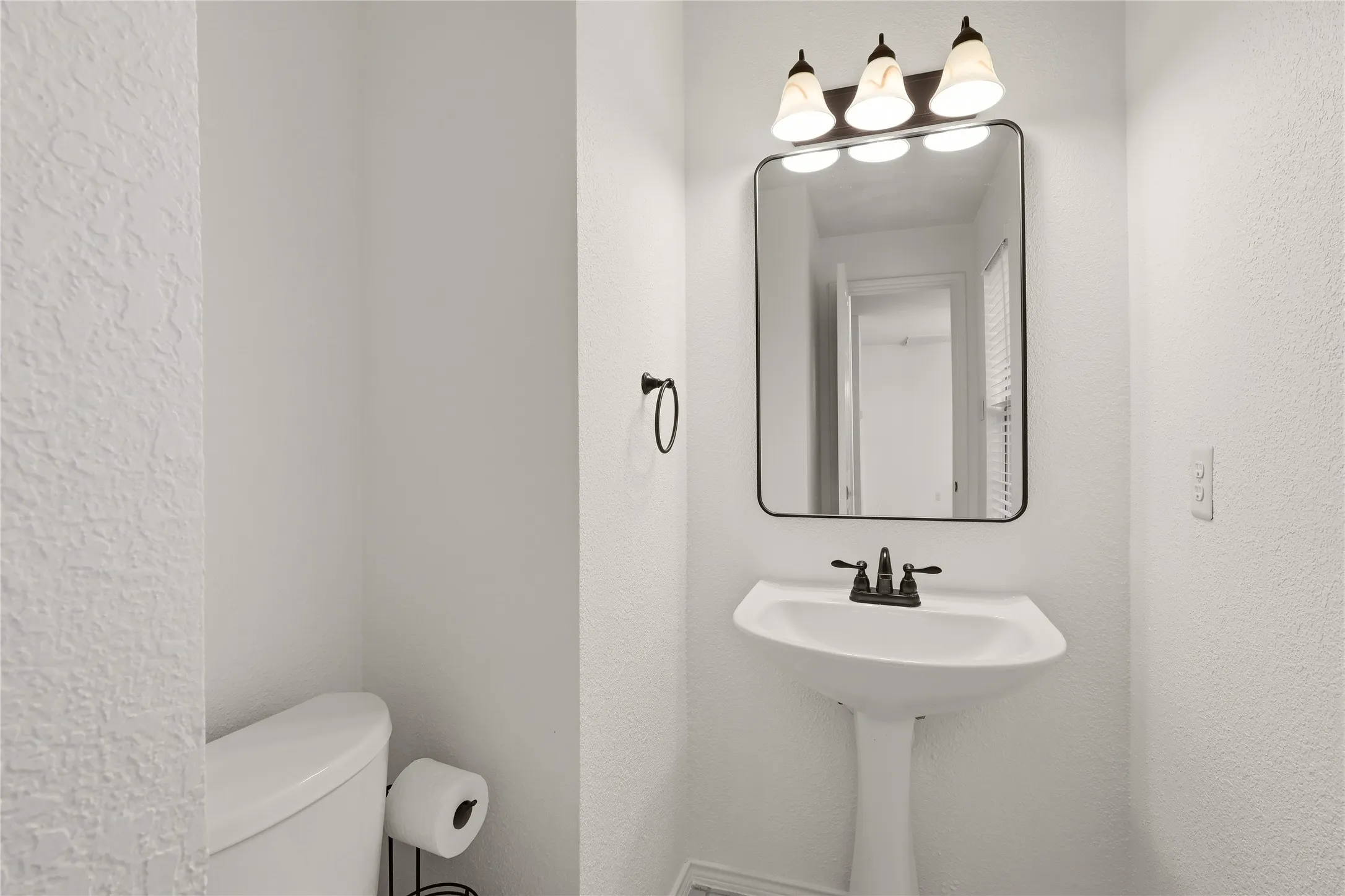 Pedestal sink with dark bronze faucet, framed mirror, and three-light vanity fixture