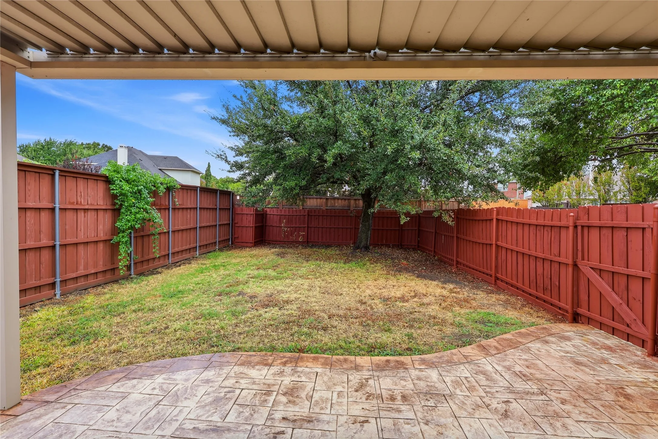Covered patio with stamped concrete flooring, red-stained privacy fence, and mature tree
