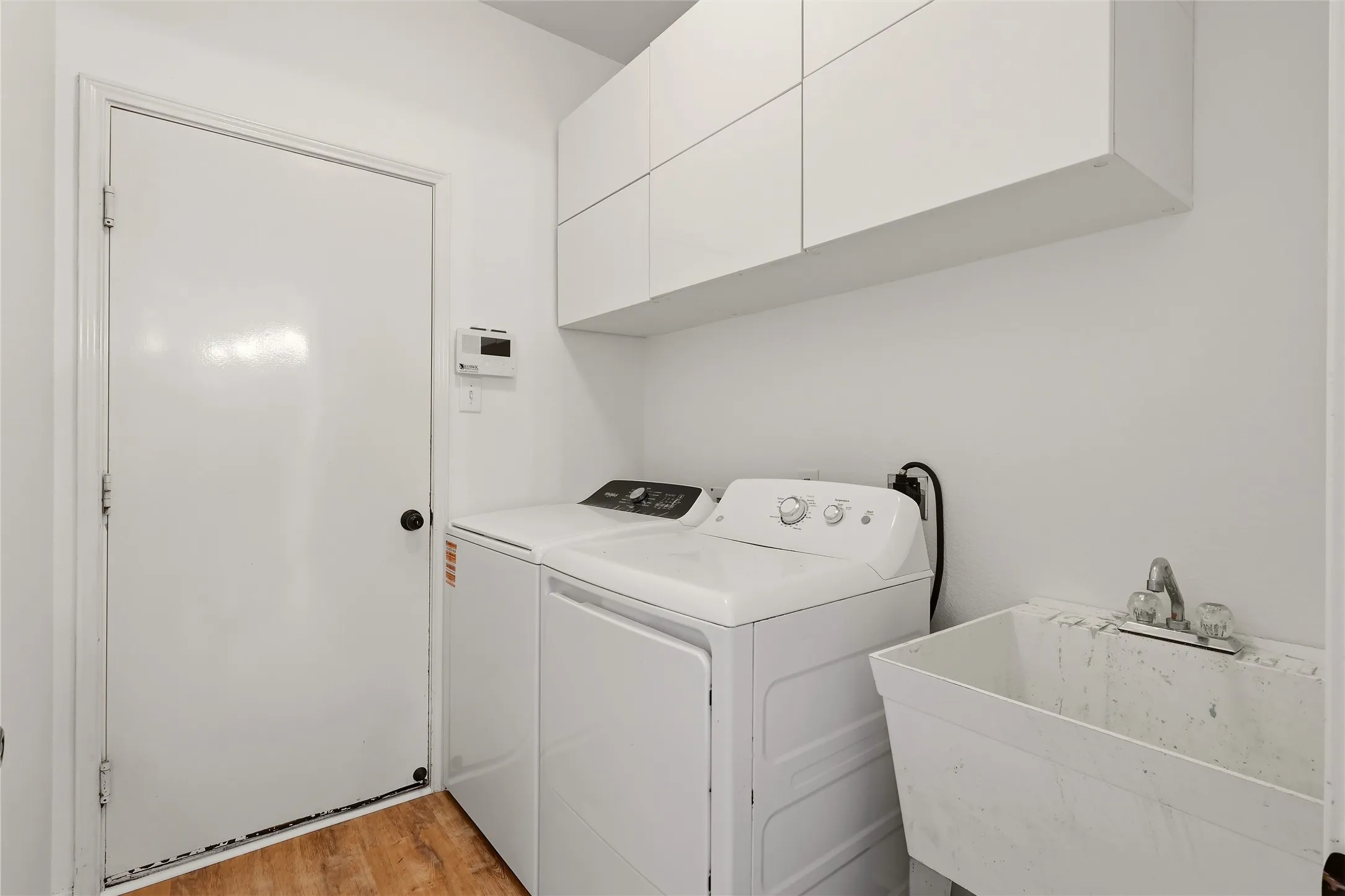 White upper cabinetry, utility sink, and wood-finish flooring